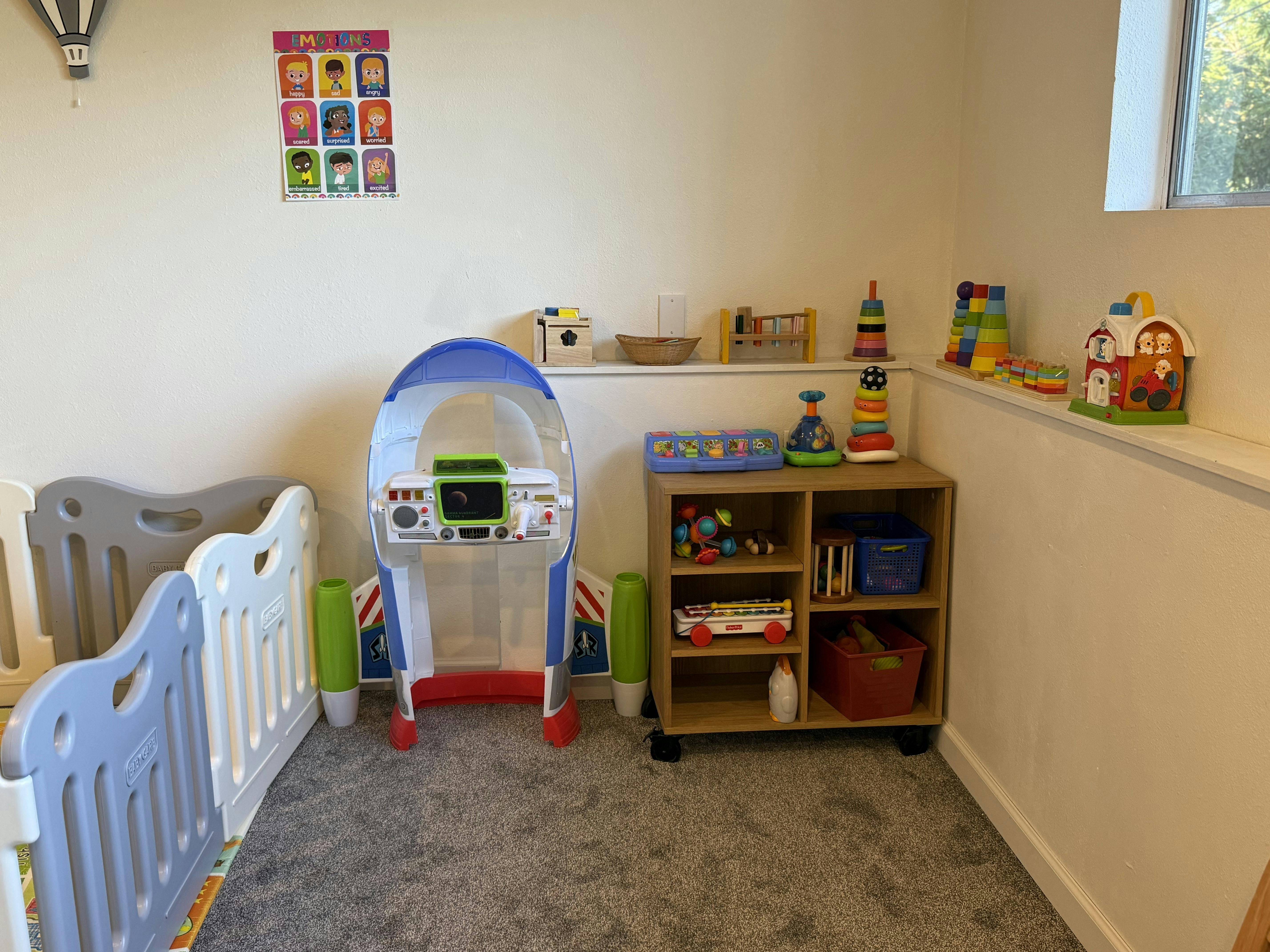 Child's play area with a toy rocket, wooden shelving unit with toys, and an emotion chart