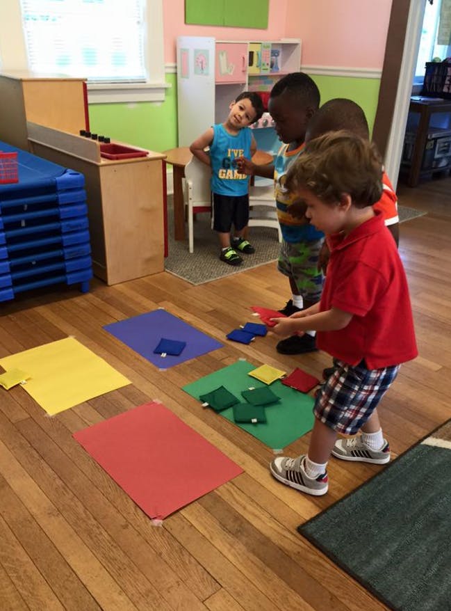 Three children playing with colorful mats and blocks on a wooden floor