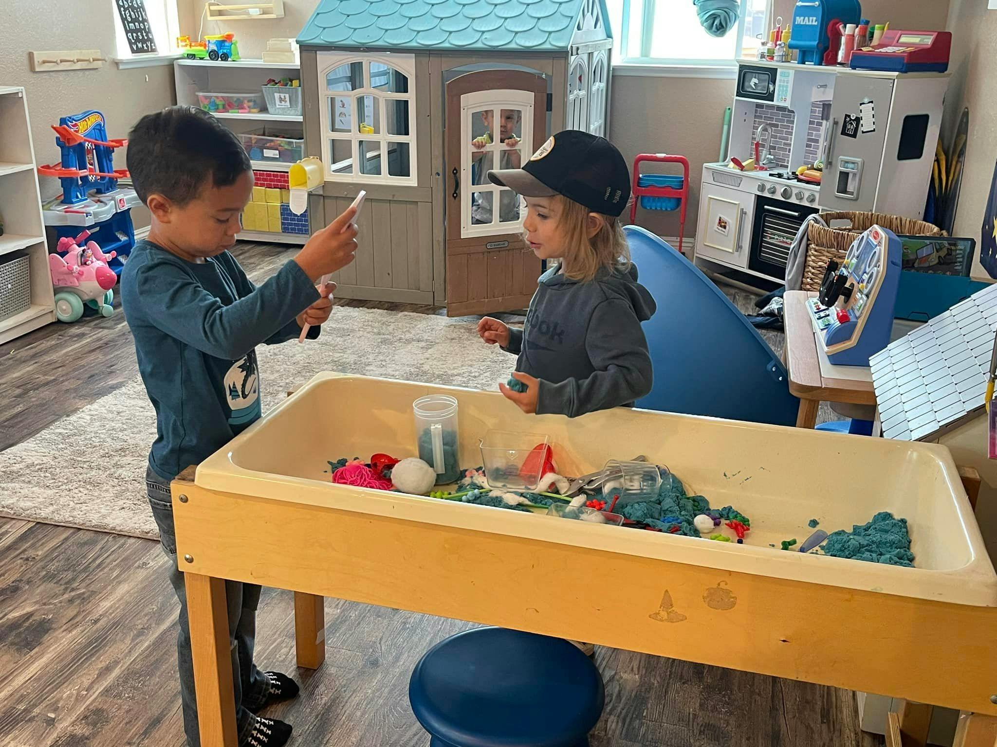 Two children playing at a sand and water table in a classroom