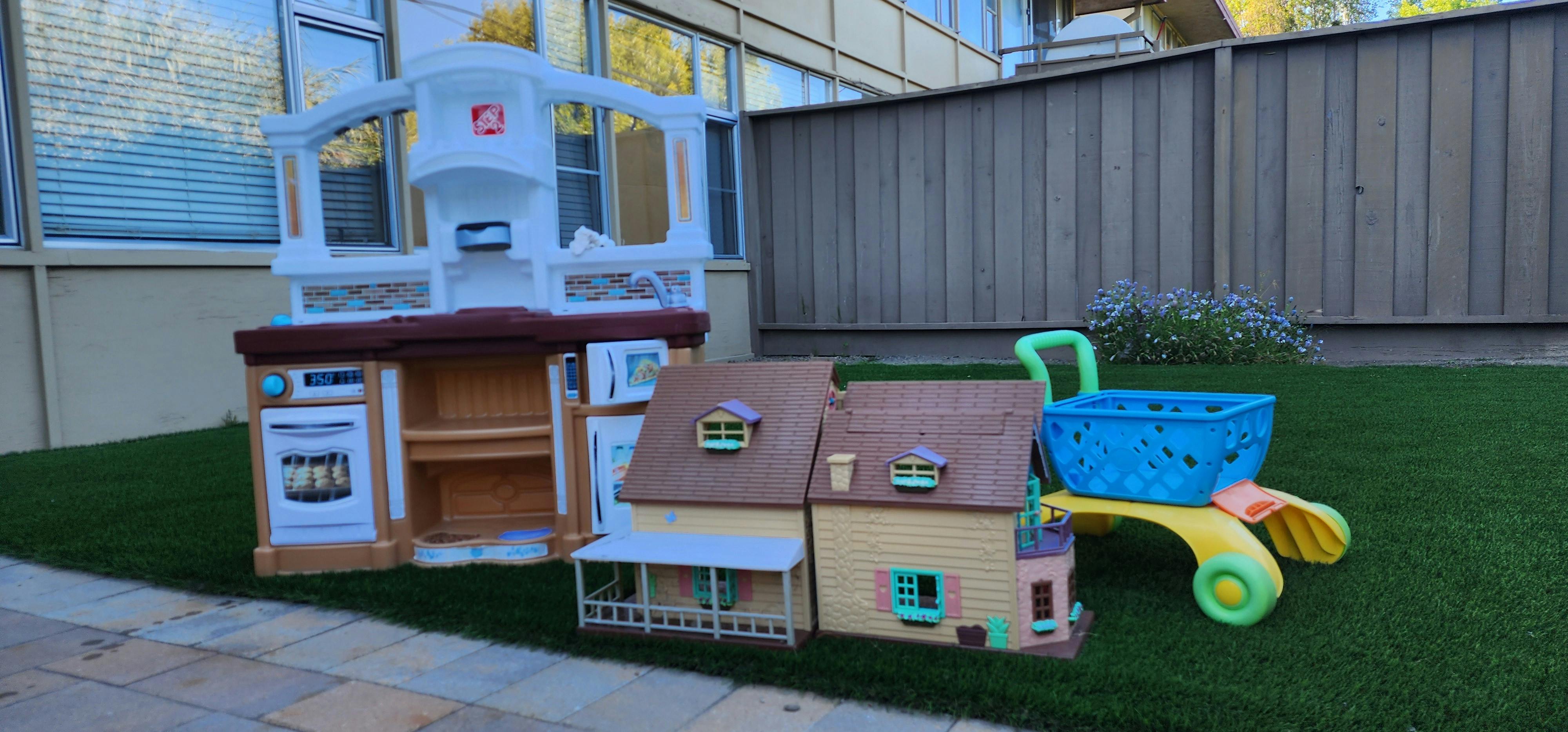 Play kitchen, dollhouse, and toy wagon on grass