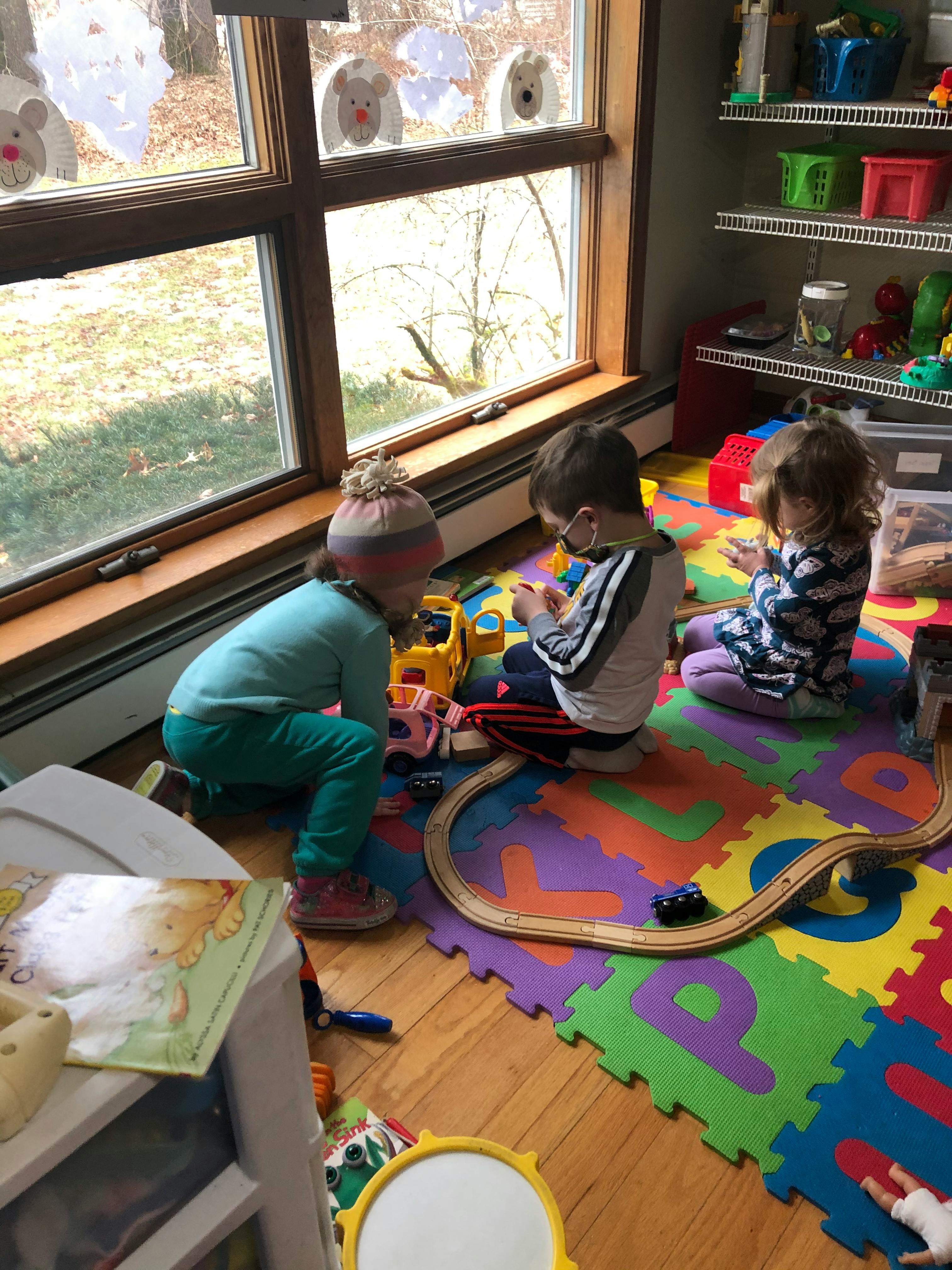 Three children playing with toys on a colorful alphabet mat