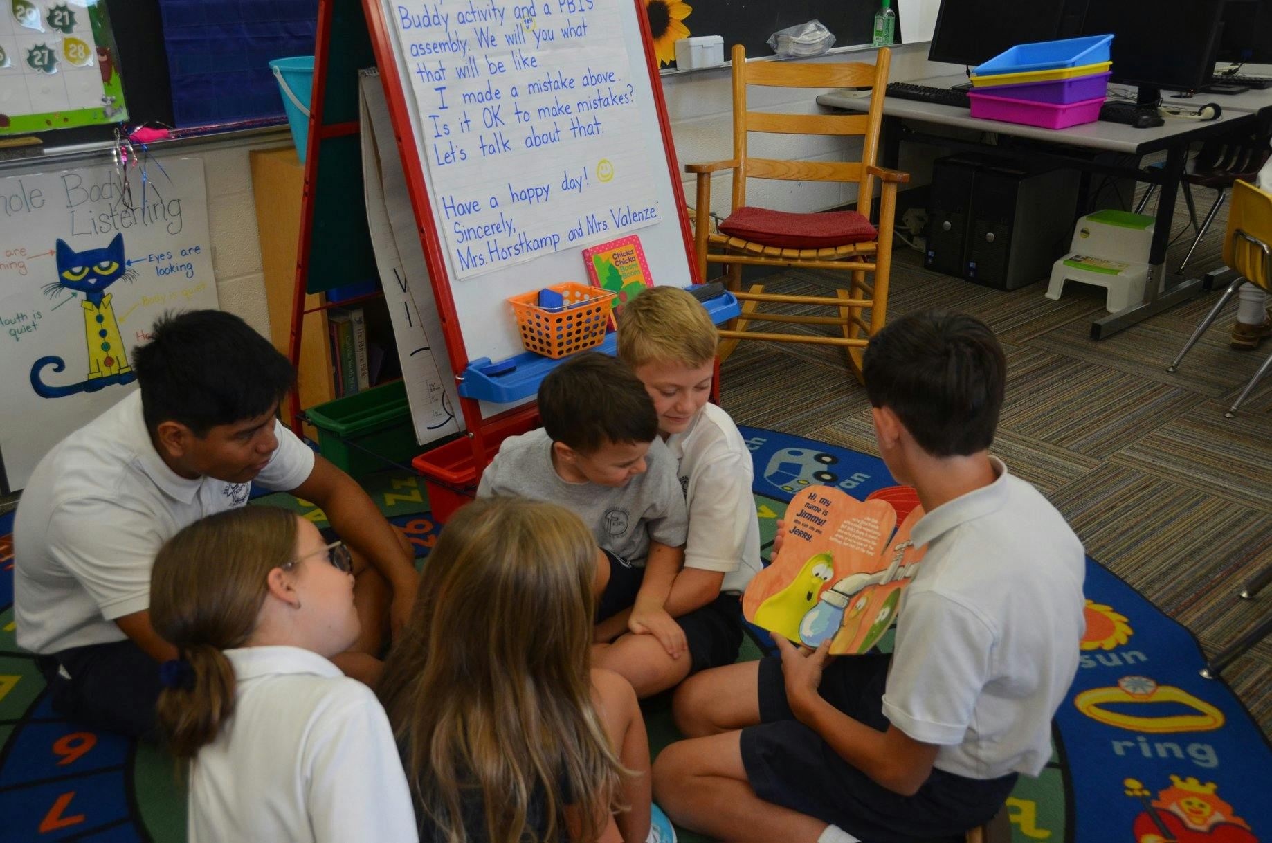 Five children and one teen sitting on a rug, looking at a book