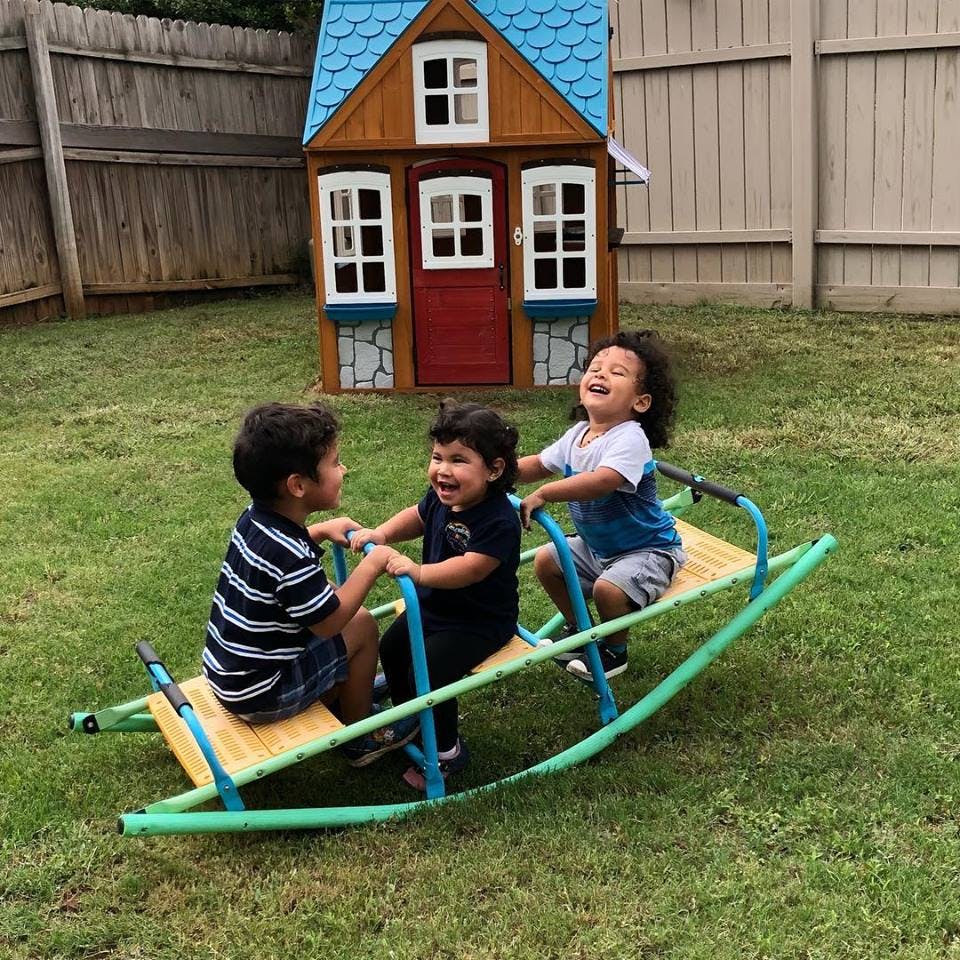 Three children on a seesaw in a yard