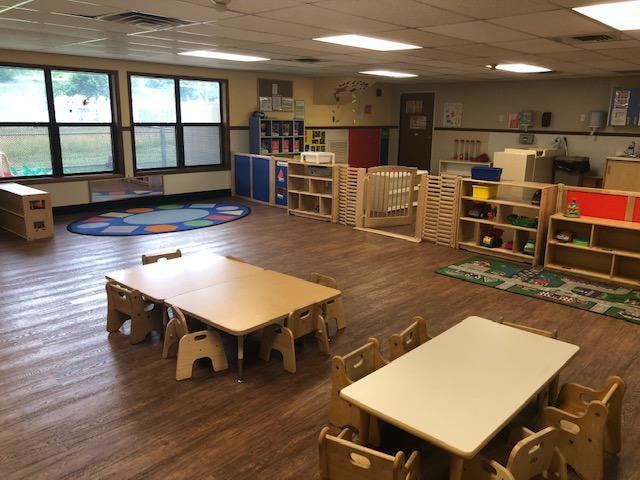Classroom with small tables and chairs, crib, shelves, and play mats