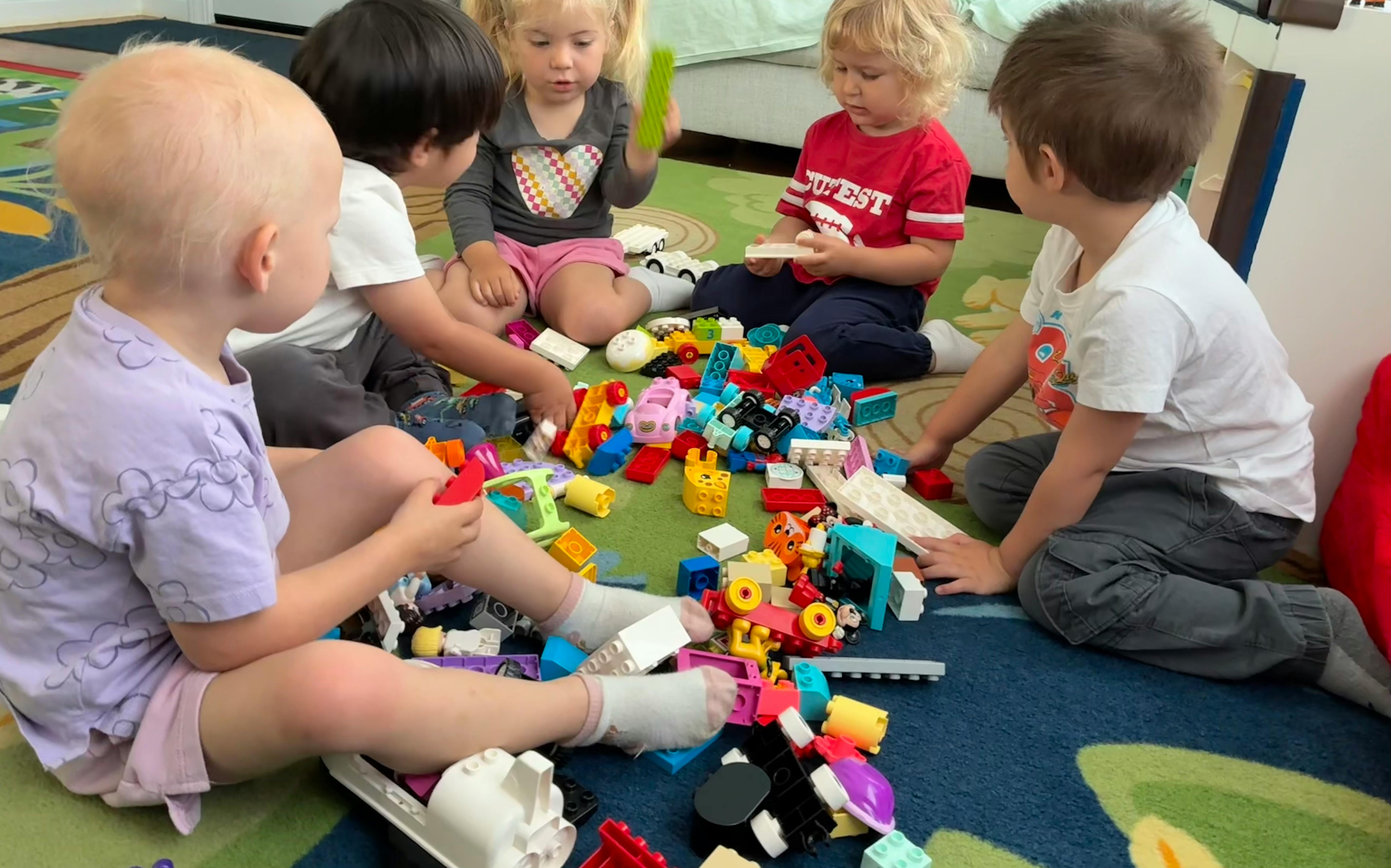 Five children playing with building blocks on a rug