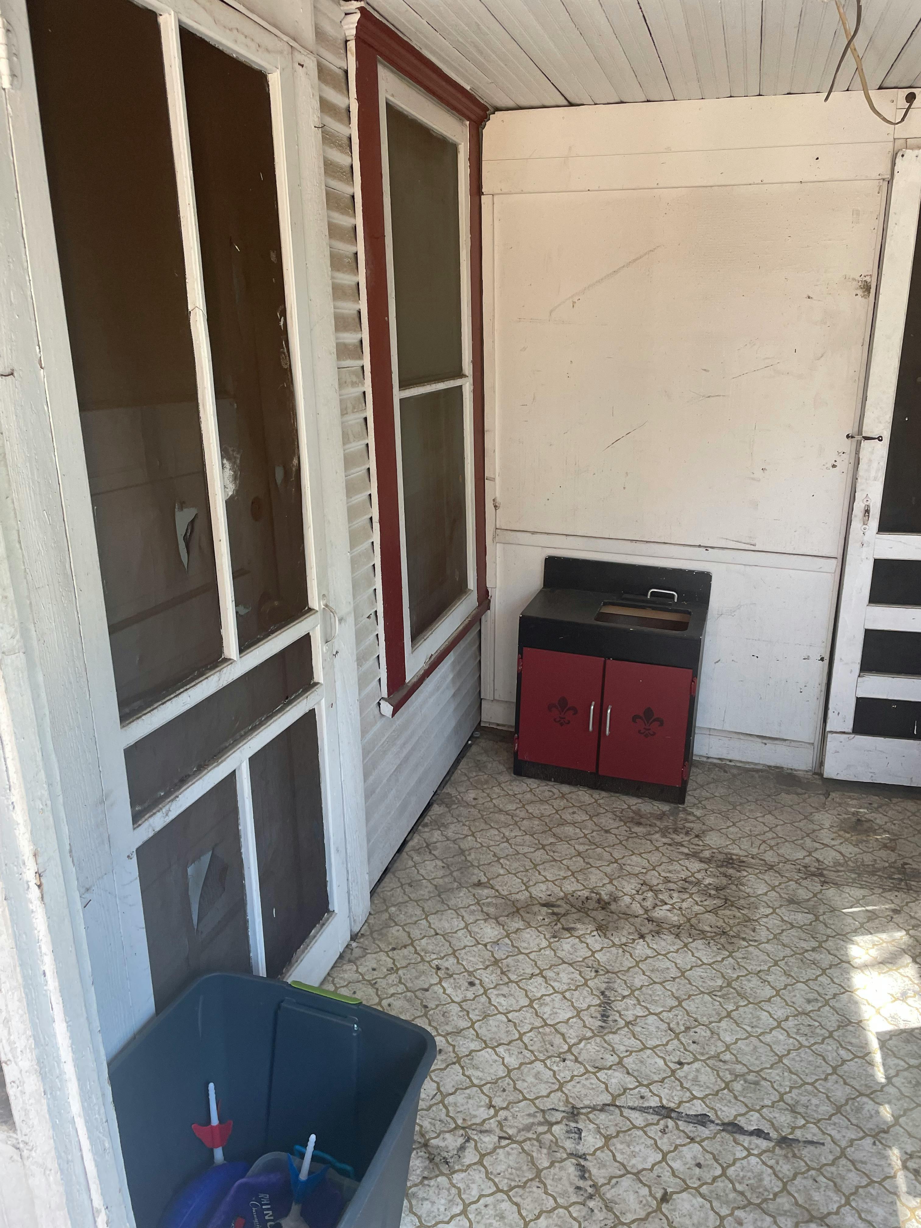 Porch with screen doors, a small cabinet, and a trash bin