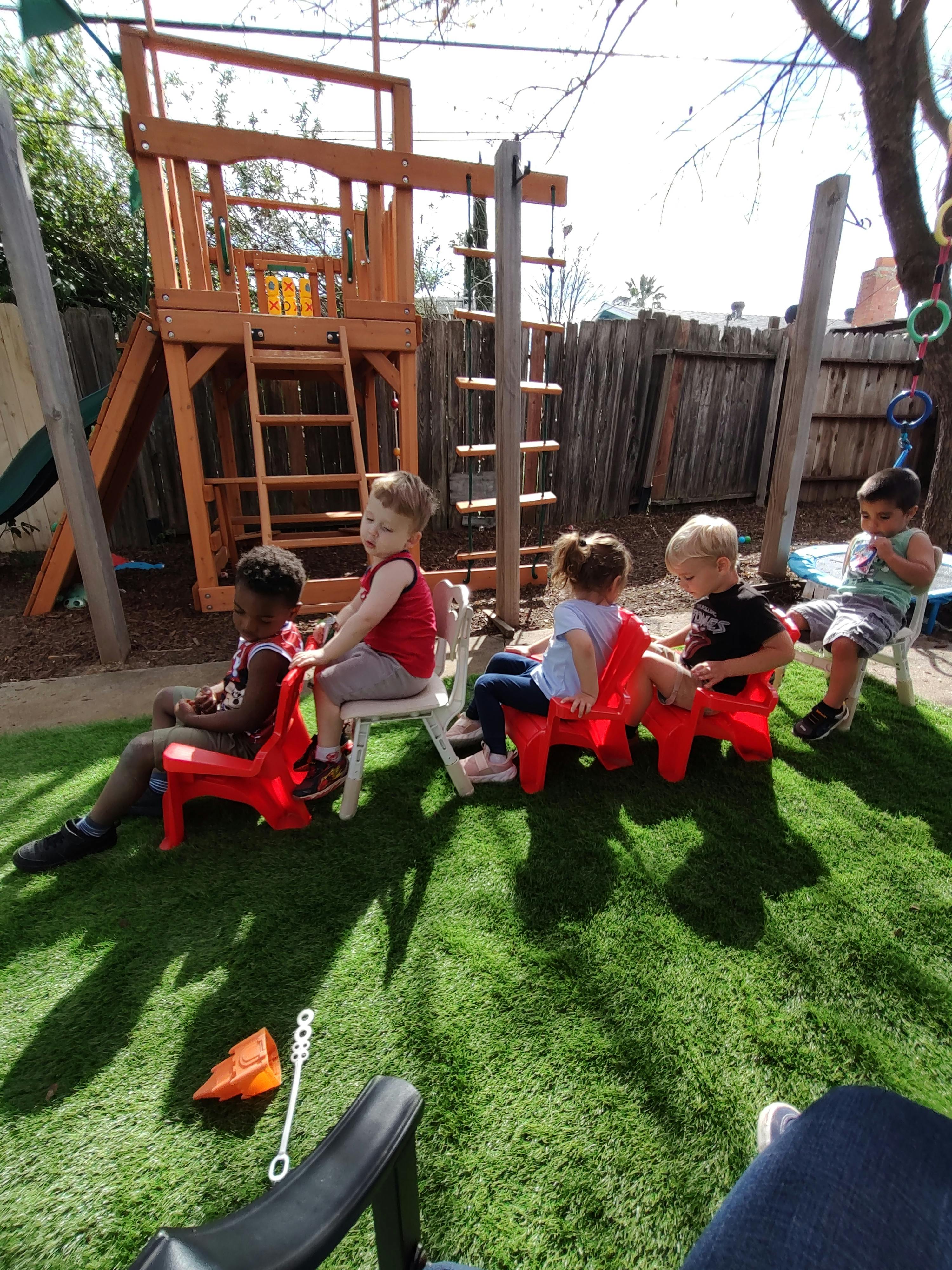 Children sitting on red chairs in a row outdoors