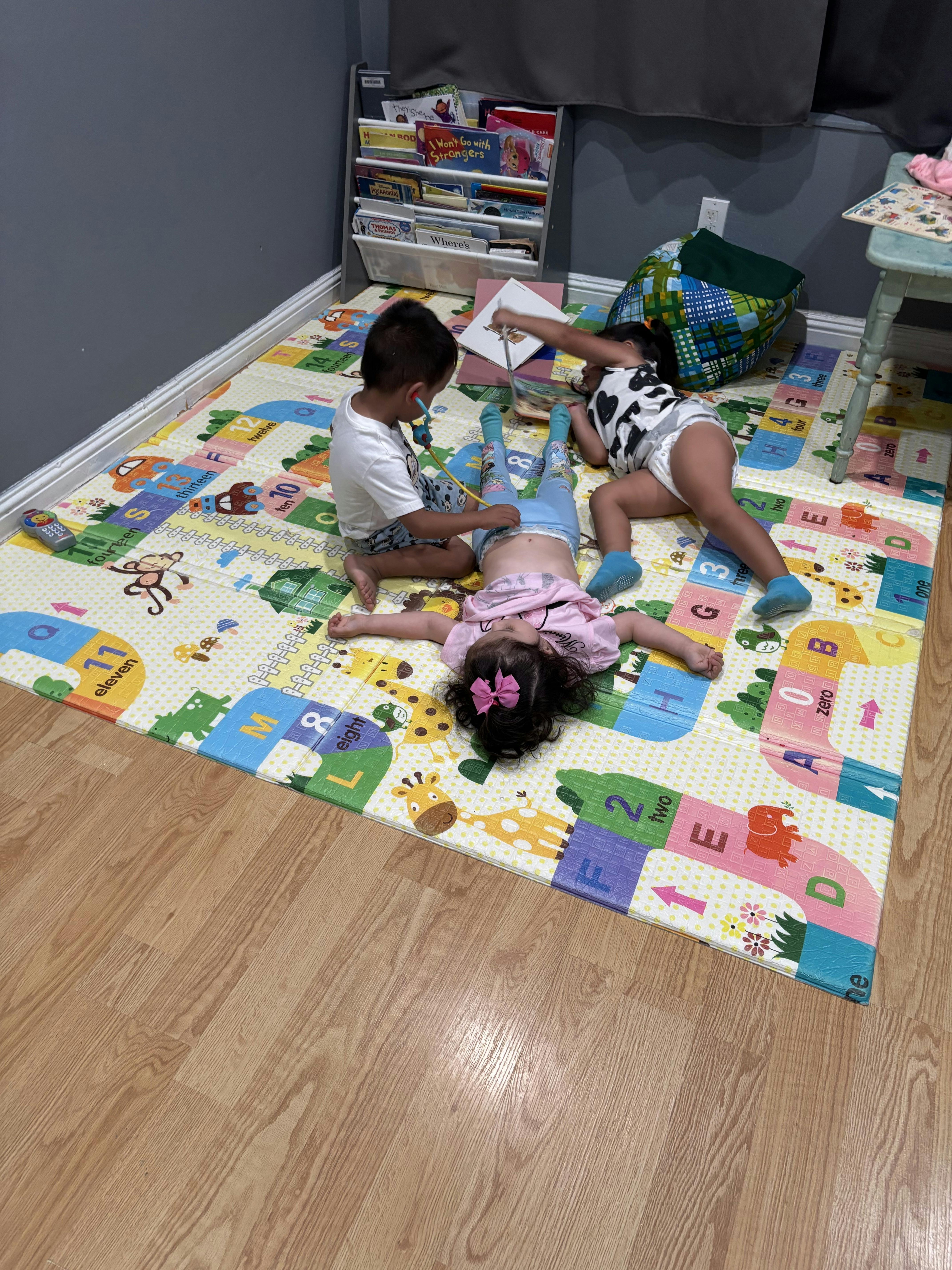 Three children playing on an alphabet mat, one with a toy stethoscope