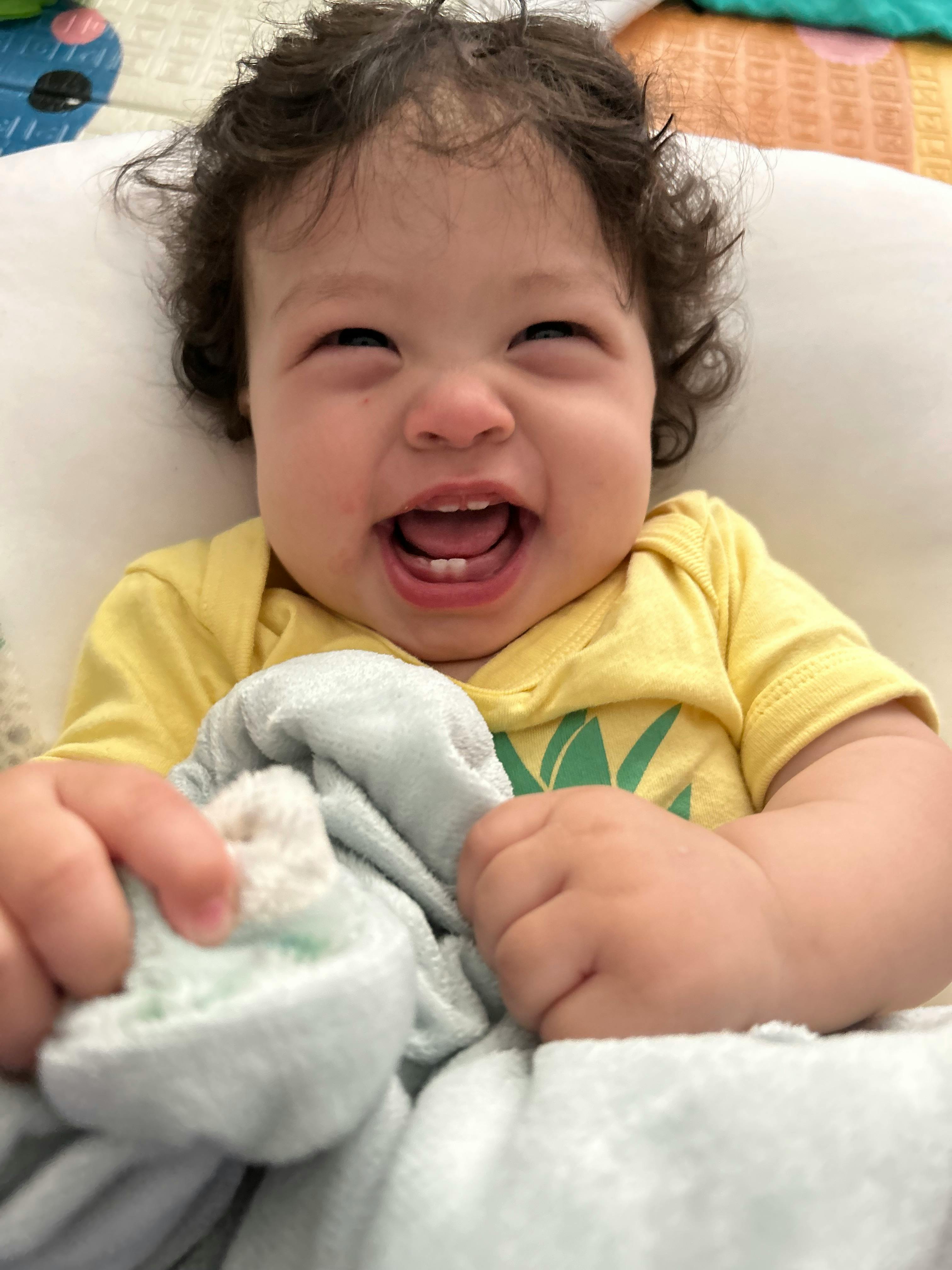 Child in yellow shirt holding a blanket and laughing