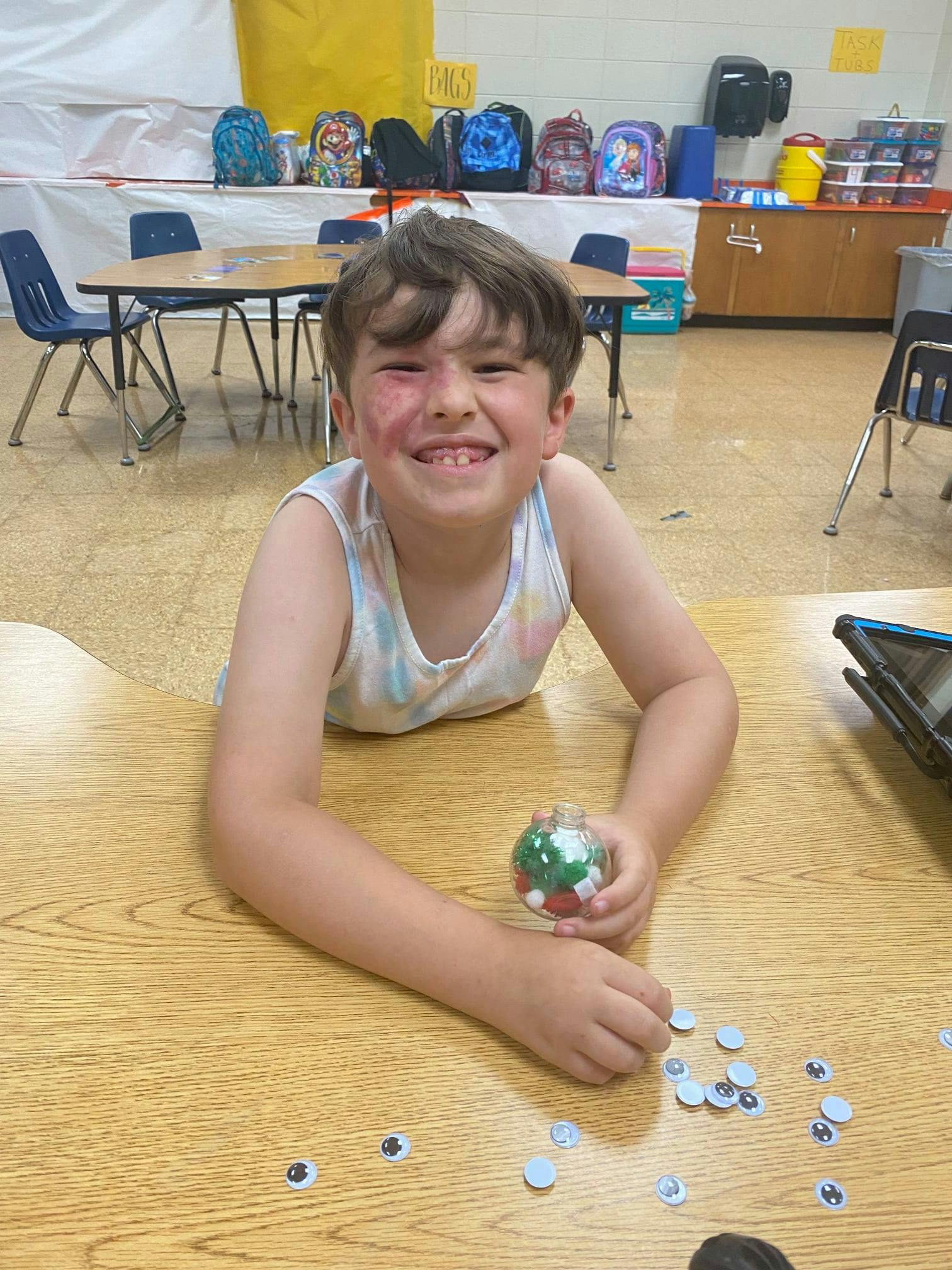Child on floor holding a small jar with googly eyes on a table