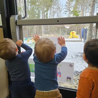 Three children looking through a glass door at an outdoor play area
