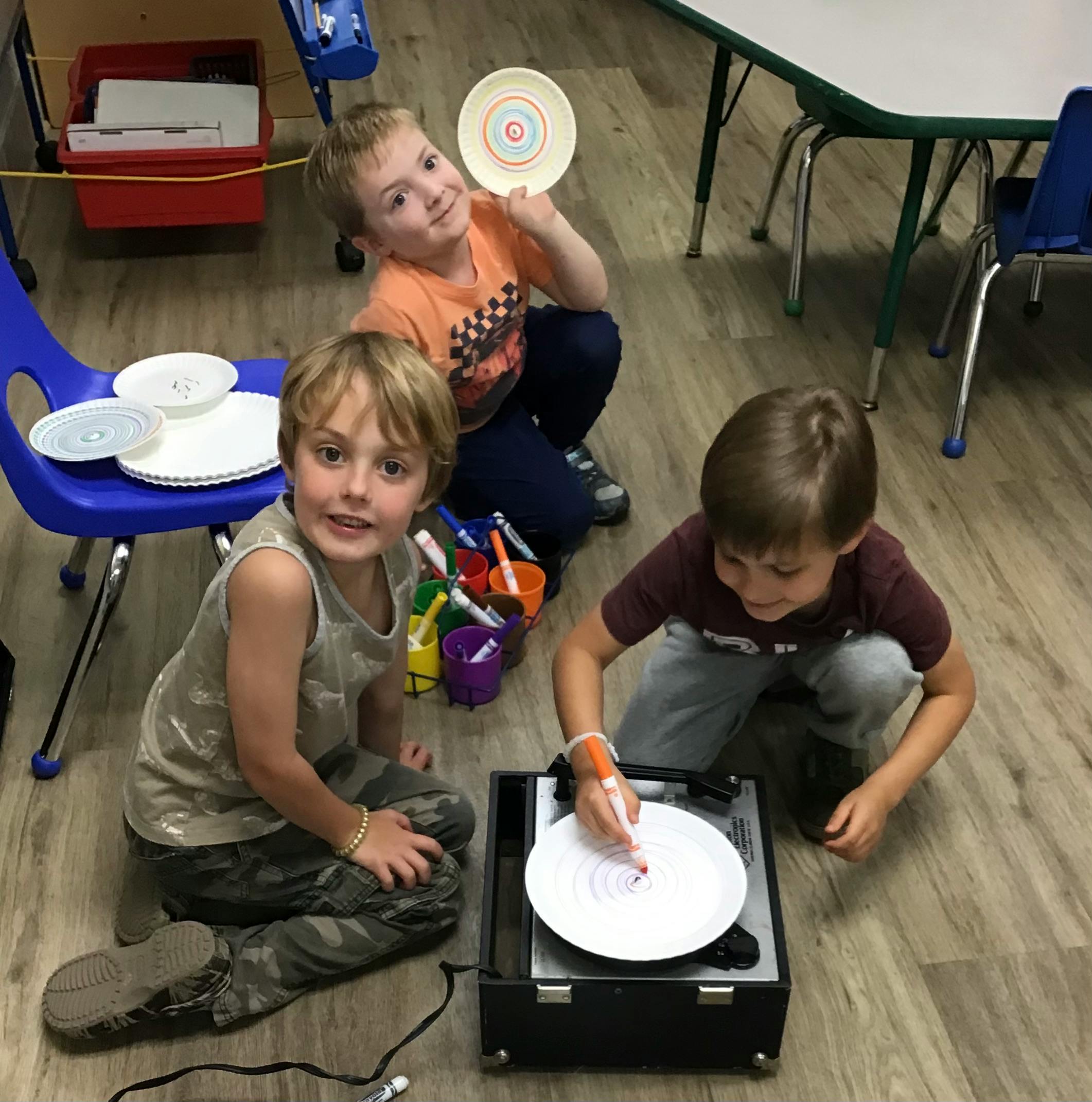 Three children on the floor, one drawing on a spinning plate