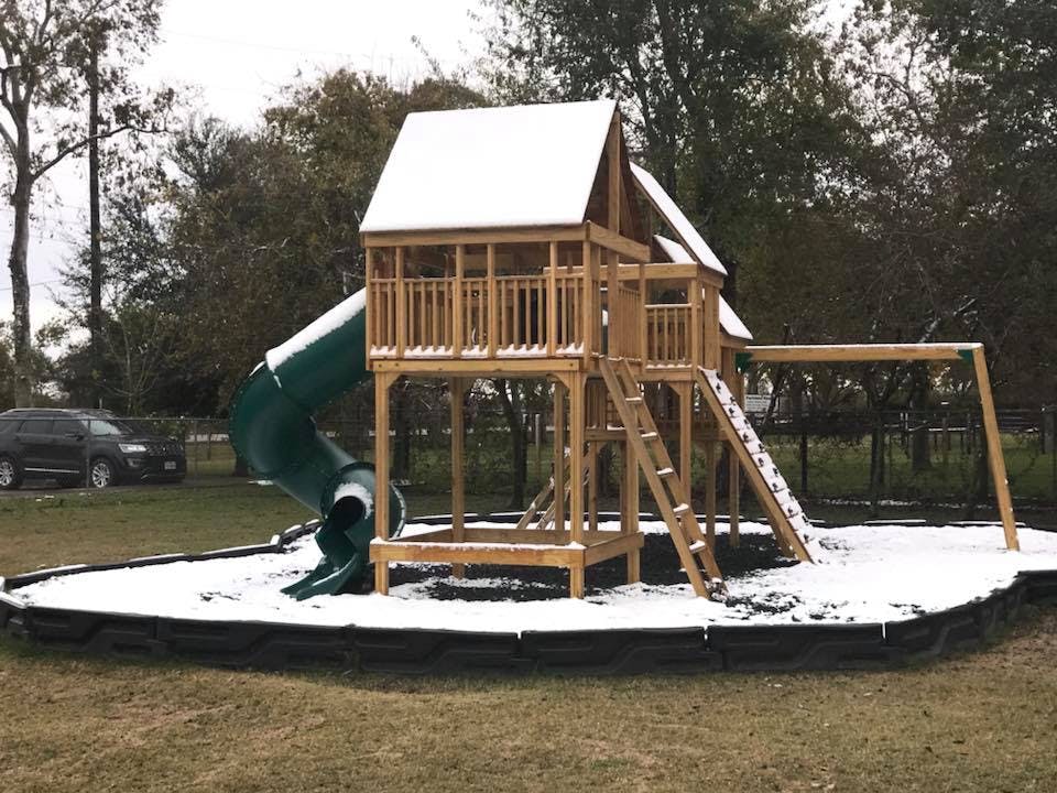 Wooden playground set with a green slide covered in a light dusting of snow