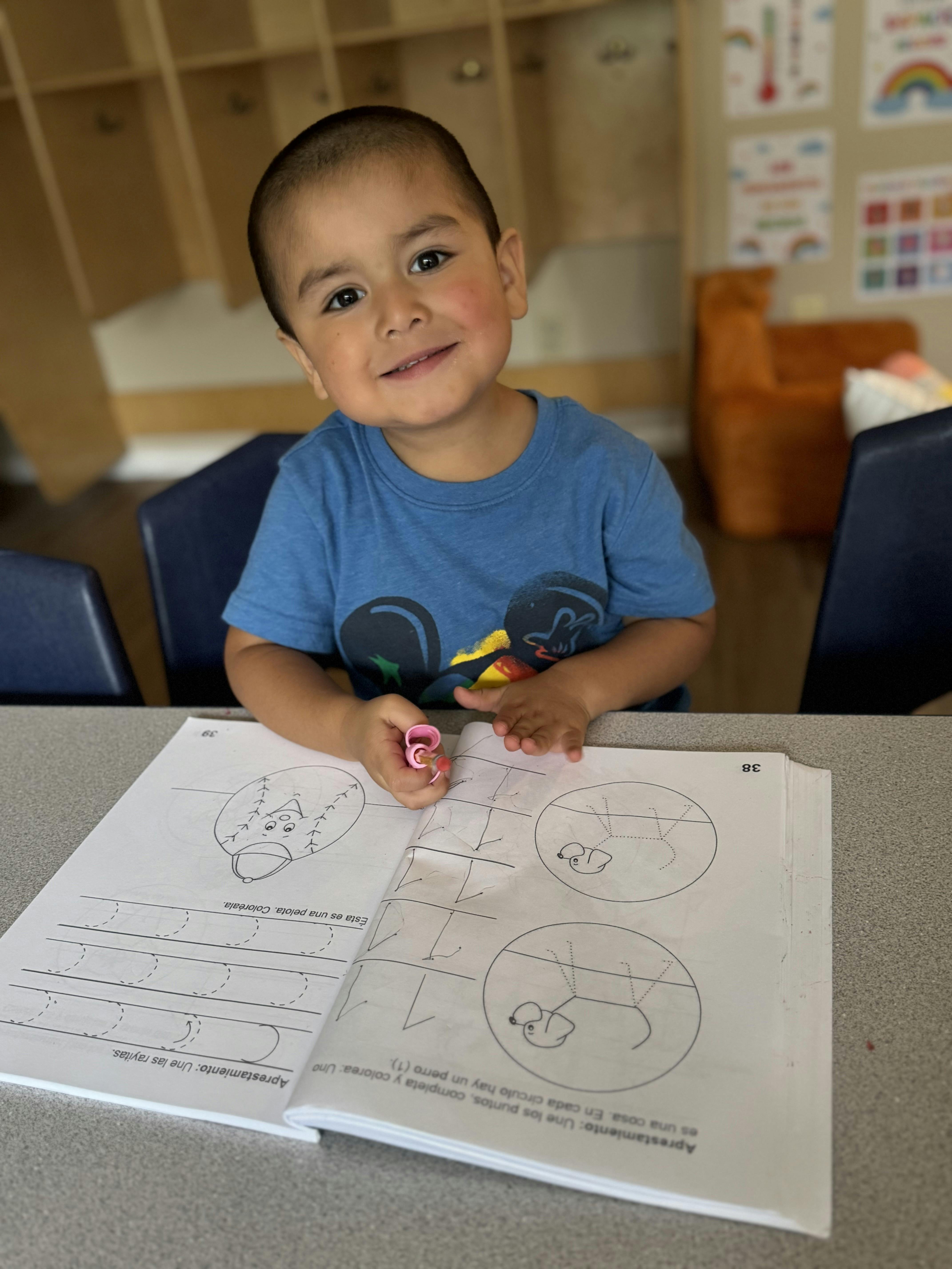 Child sitting at a table with an open workbook and a pink marker