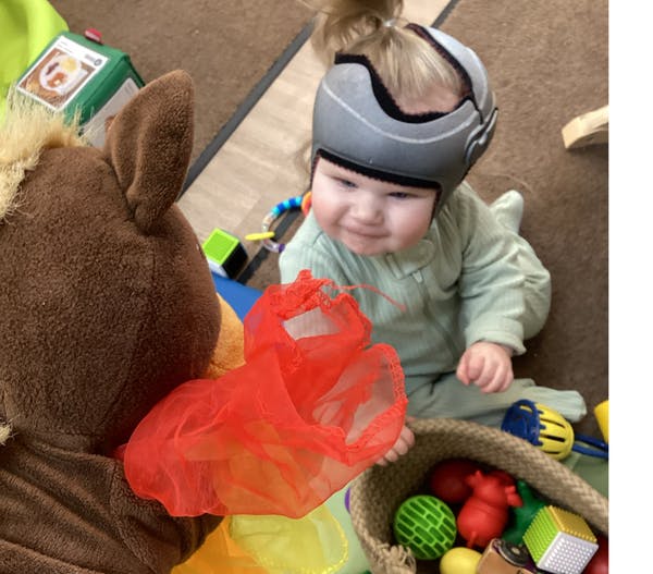 Child wearing a helmet, sitting on the floor with toys