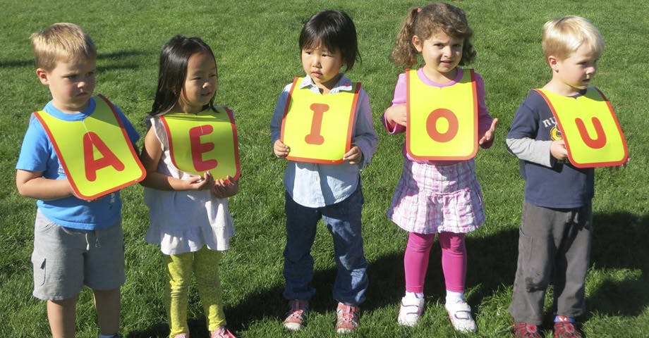 Five children standing in a line holding signs with letters A, E, I, O, U