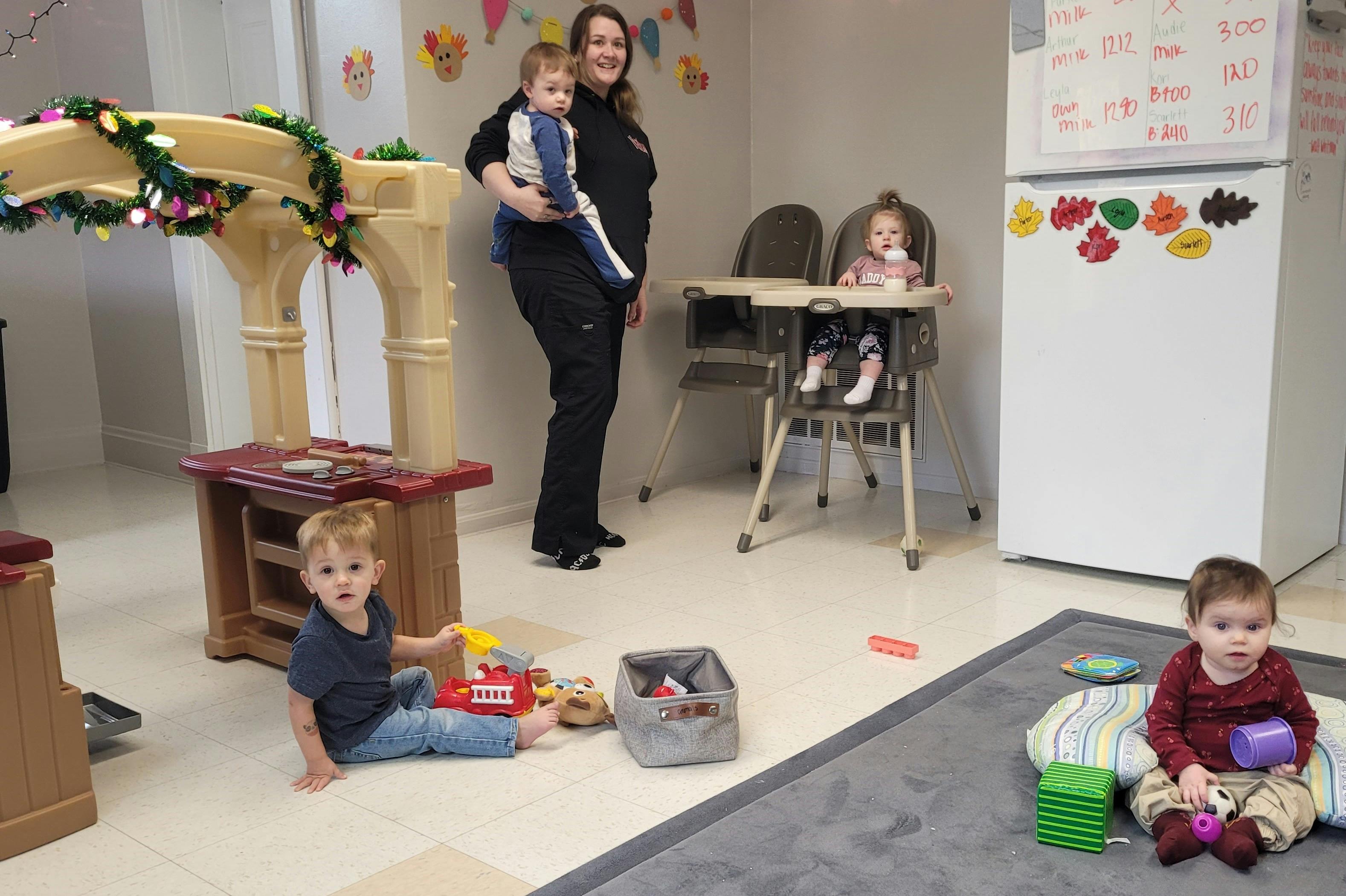 Adult holding a child in a room with three other children playing