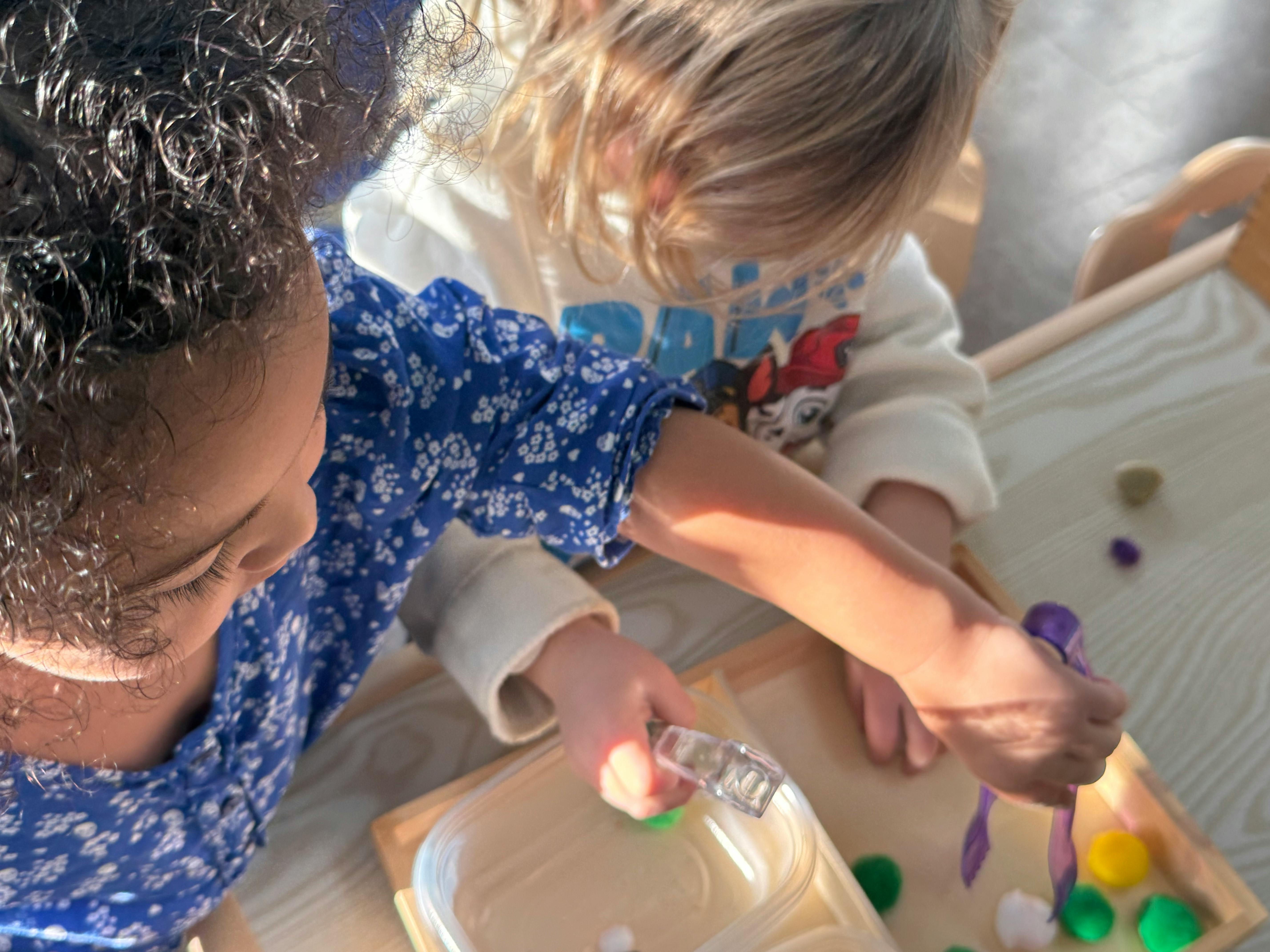 Two children playing with colorful pom-poms and a spray bottle