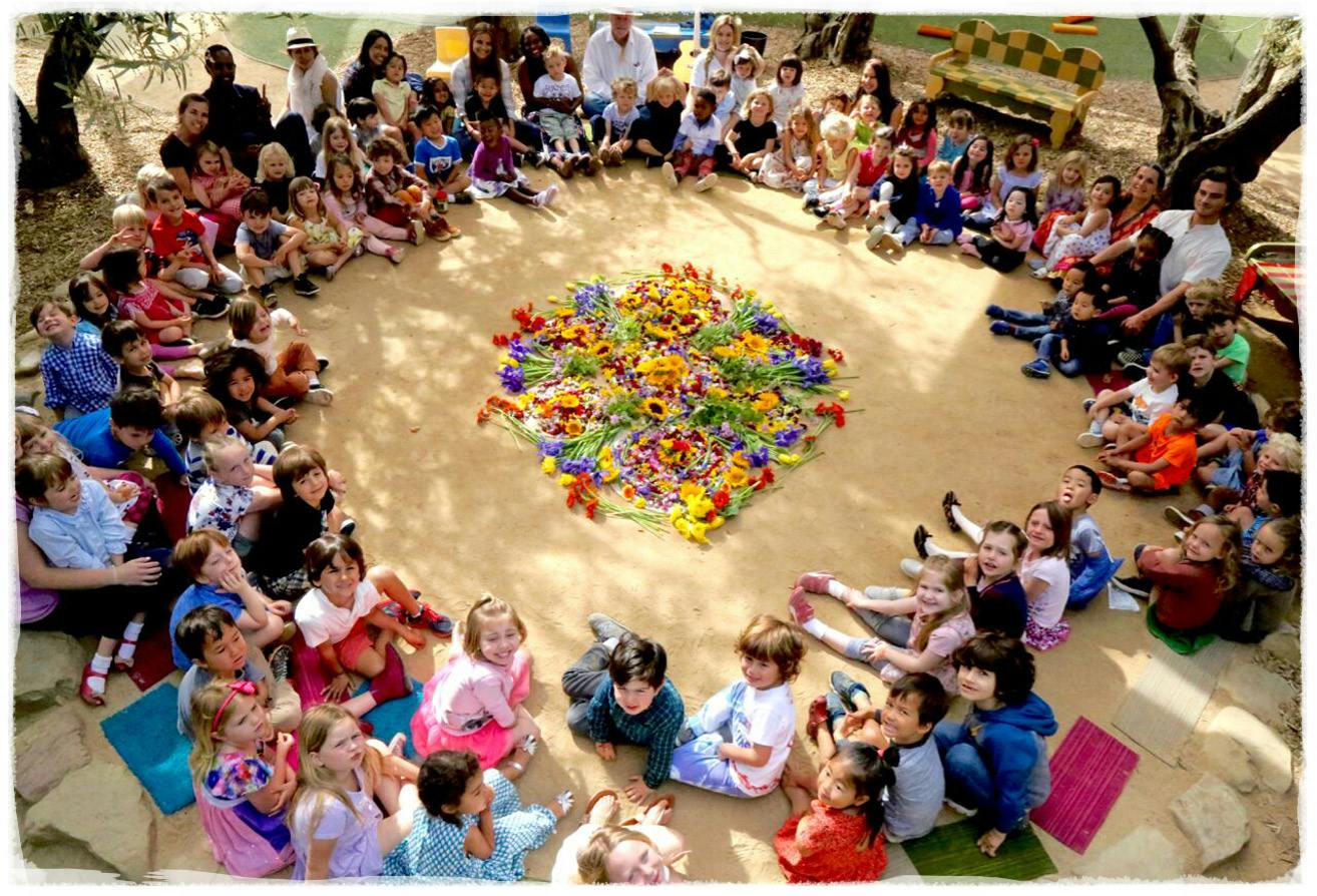 Group of children and adults sitting in a circle around a large flower arrangement