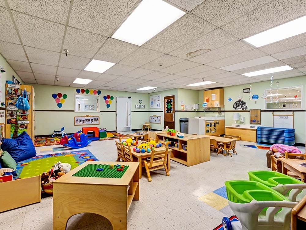 Preschool classroom with tables, chairs, toys, and colorful decorations