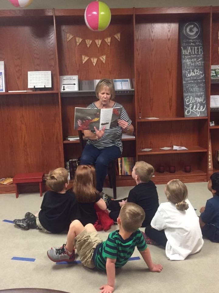 Adult reading a book to children sitting on the floor in a classroom