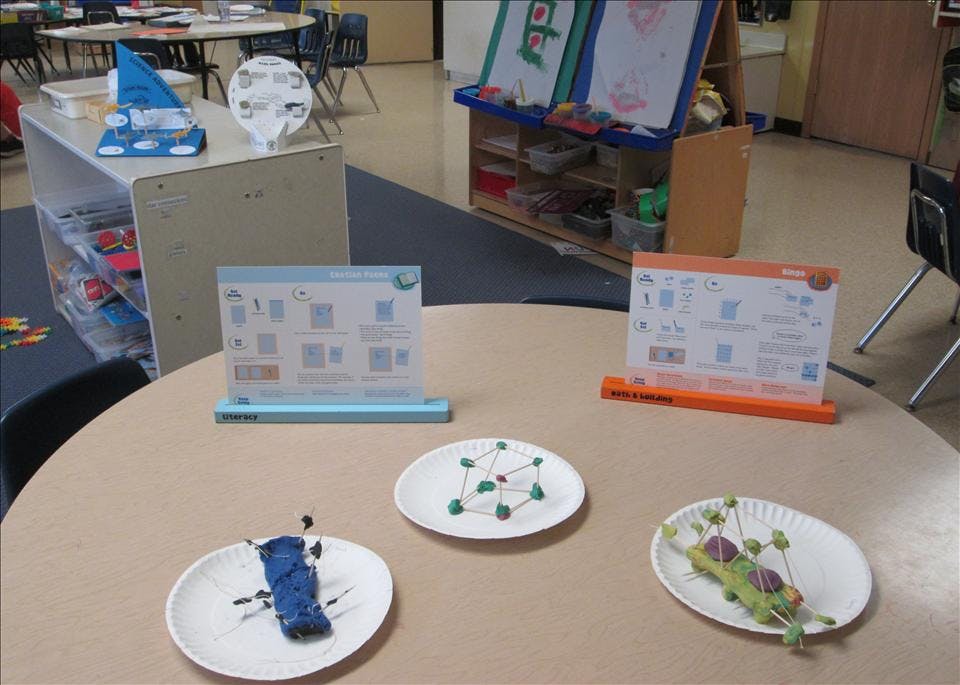 Classroom table with science project instructions and student creations on plates