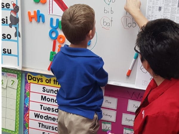Child and person writing on a whiteboard in a classroom