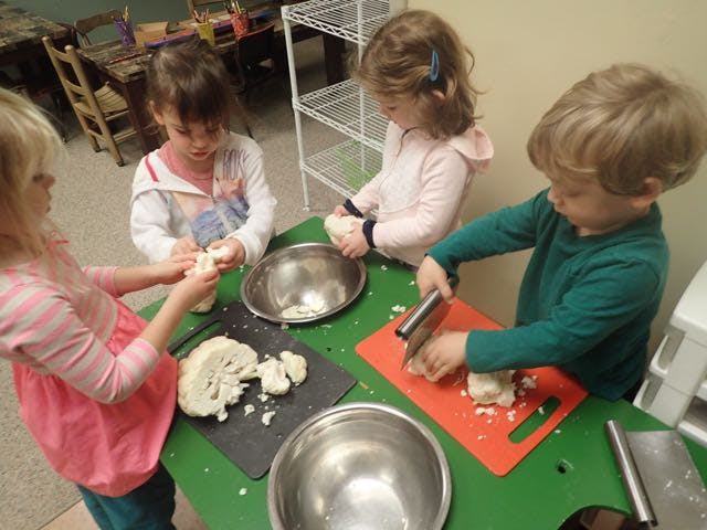 Four children preparing cauliflower on a green table