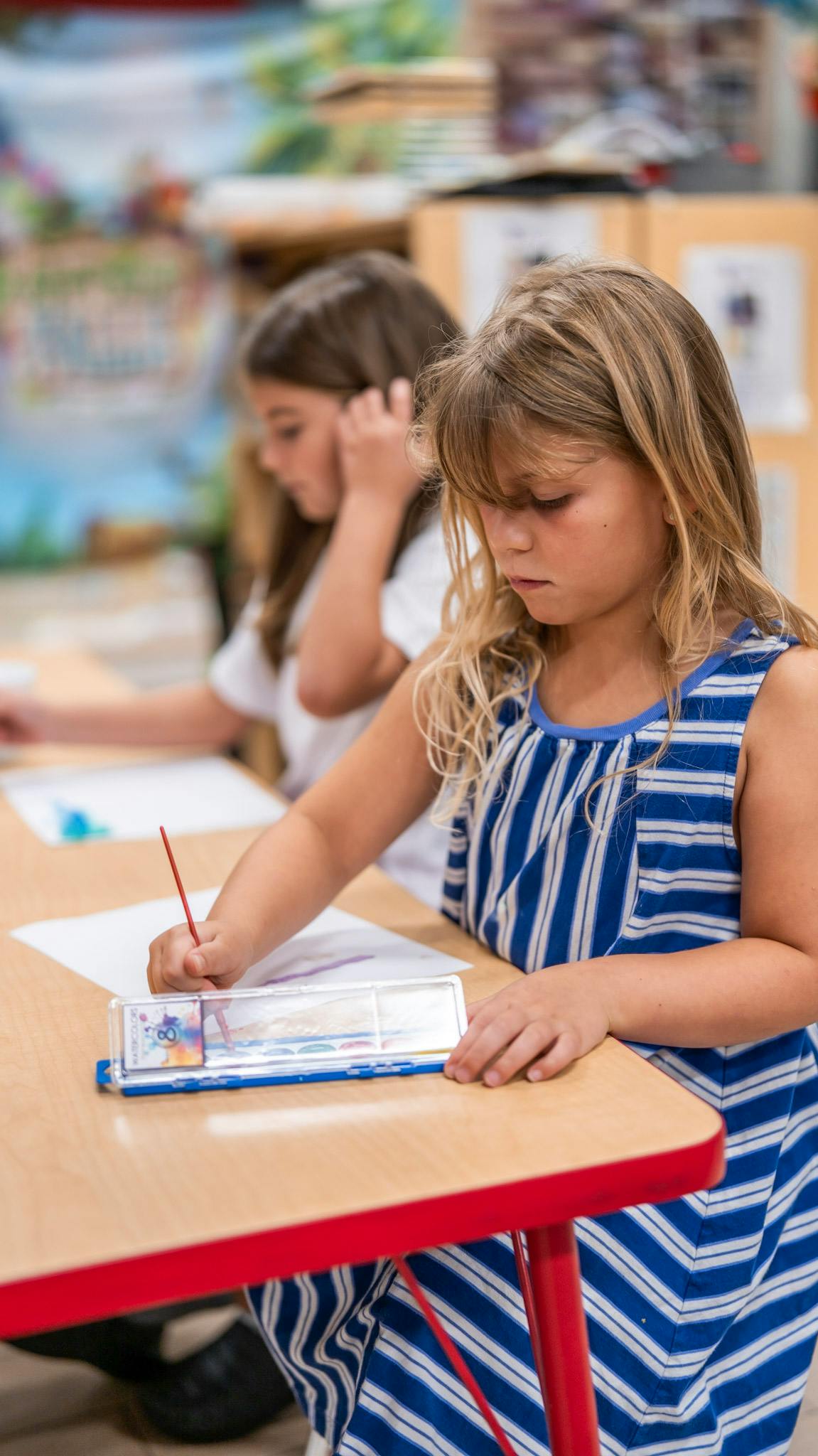 Child using a paintbrush to paint on paper at a desk
