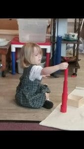 Child playing with a red cylinder toy on the floor