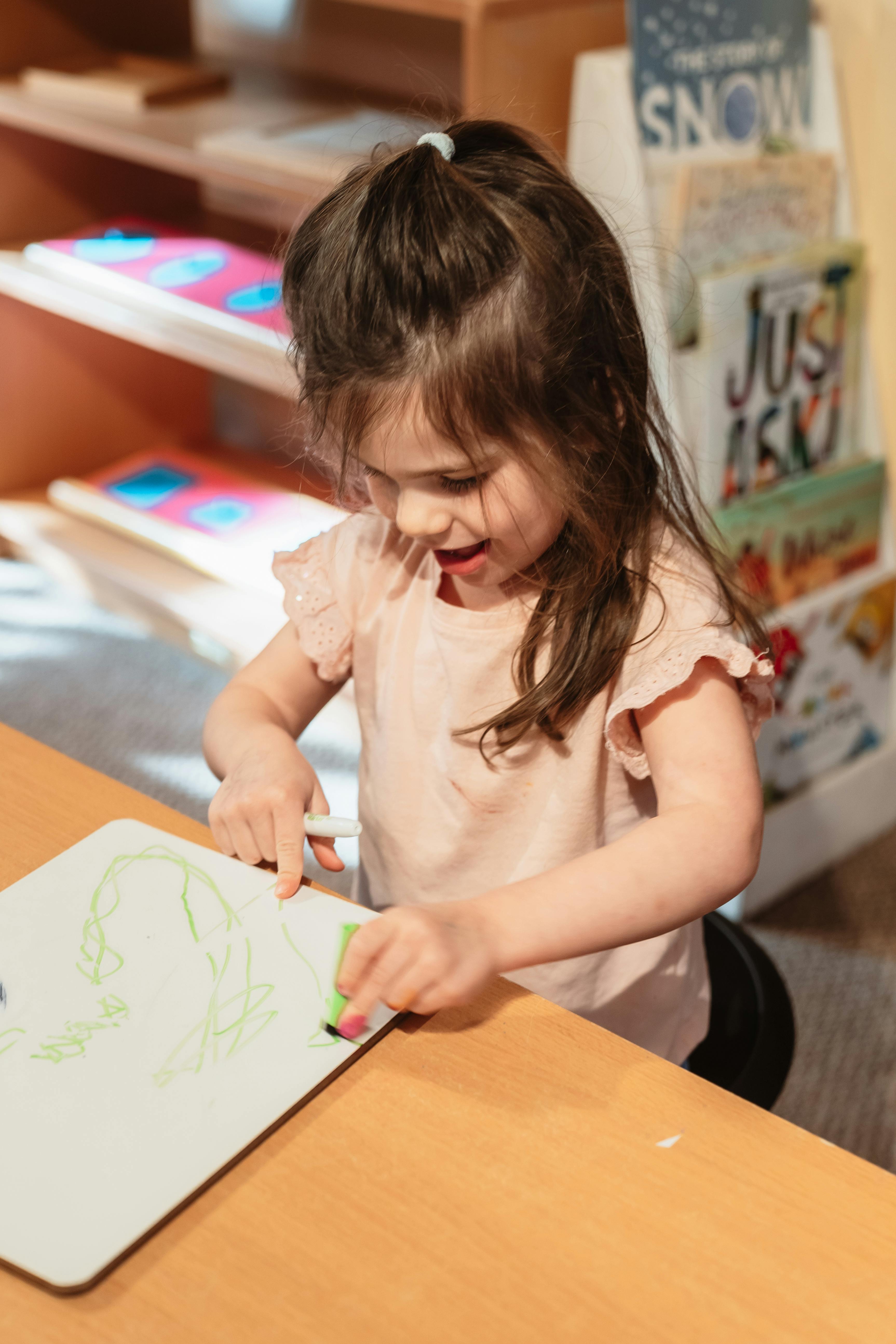 Child drawing on a whiteboard with a green marker