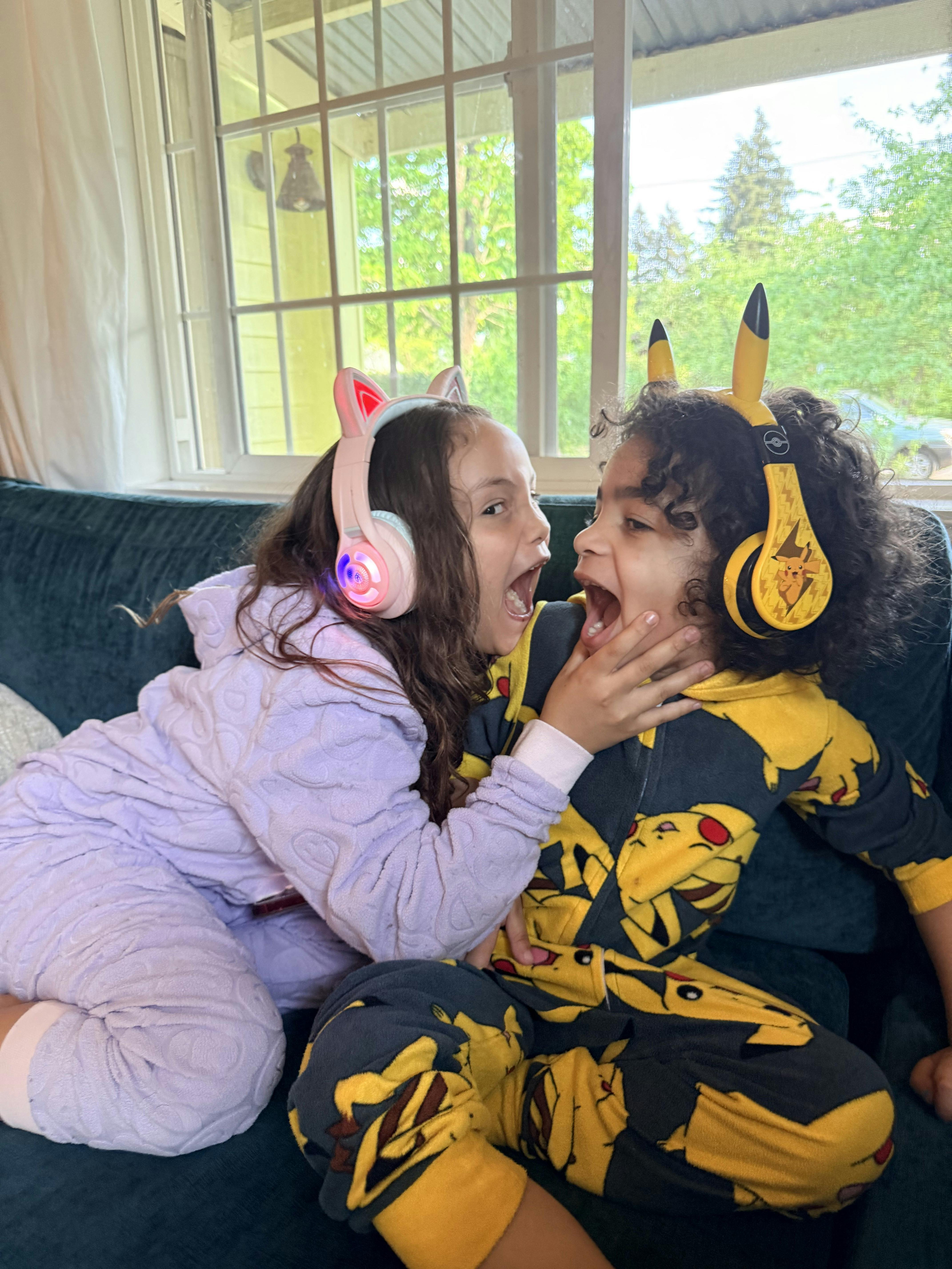 Child wearing cat headphones with glowing ears and child in Pikachu headphones playing together