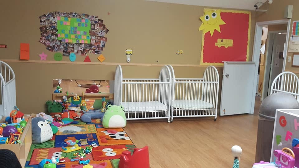 Two white cribs in a room with toys on a colorful rug