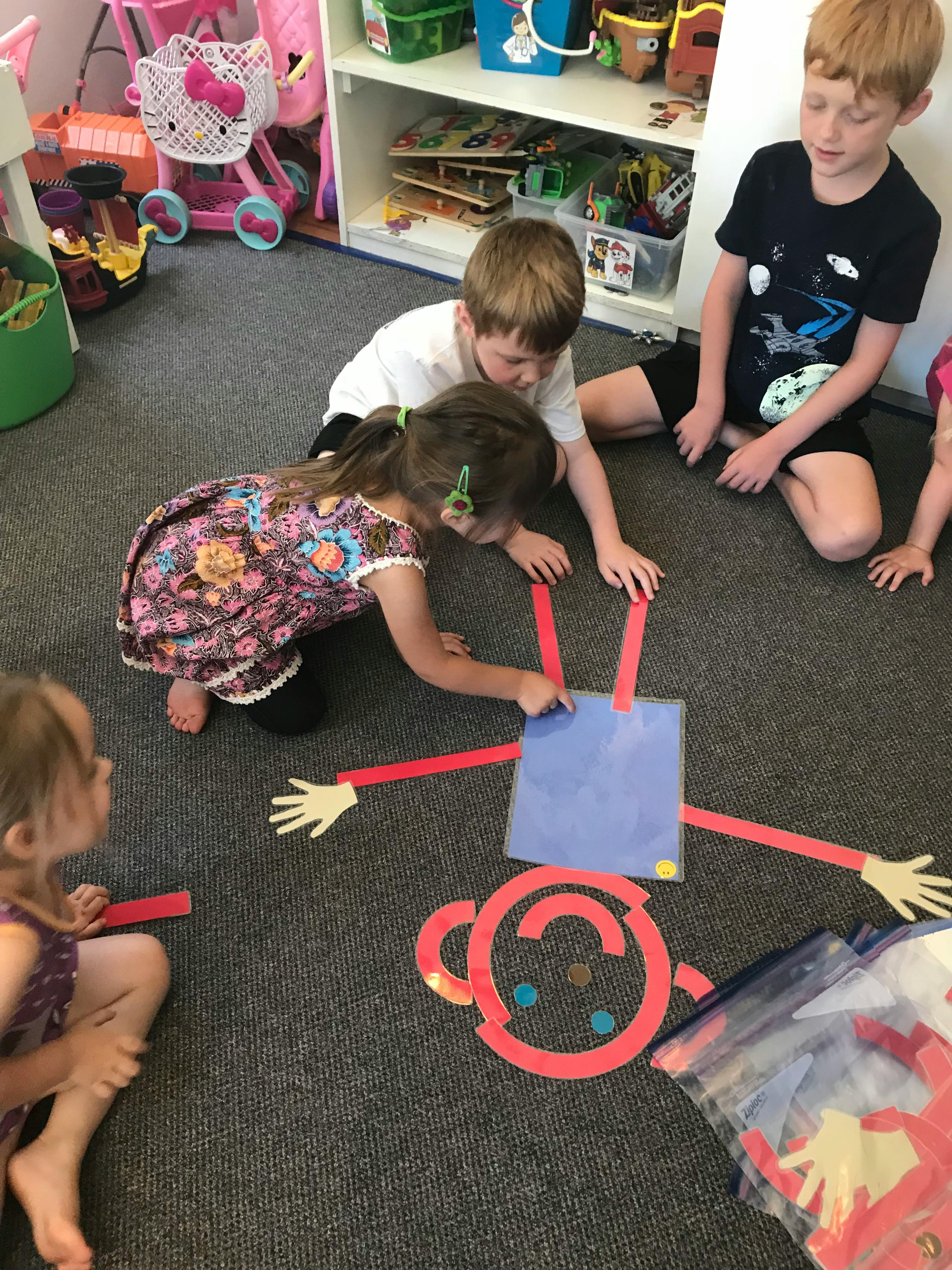Children sitting on a floor arranging paper body parts to build a figure