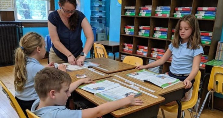 Adult and three children at desks in a classroom