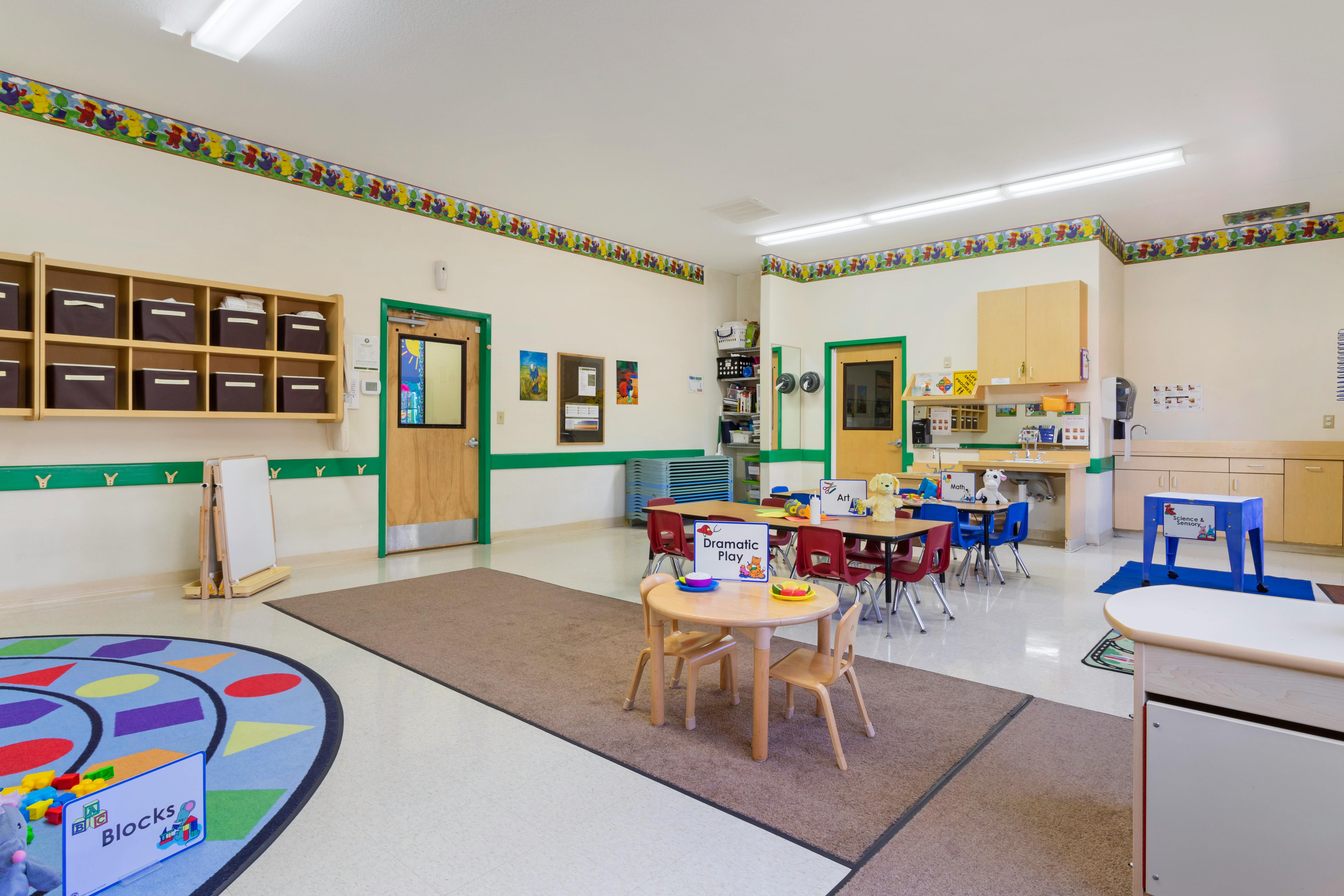 Classroom with child-sized tables and chairs, play mats, and learning stations
