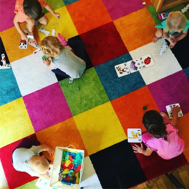 Multiple children playing with toys on a colorful checkered rug