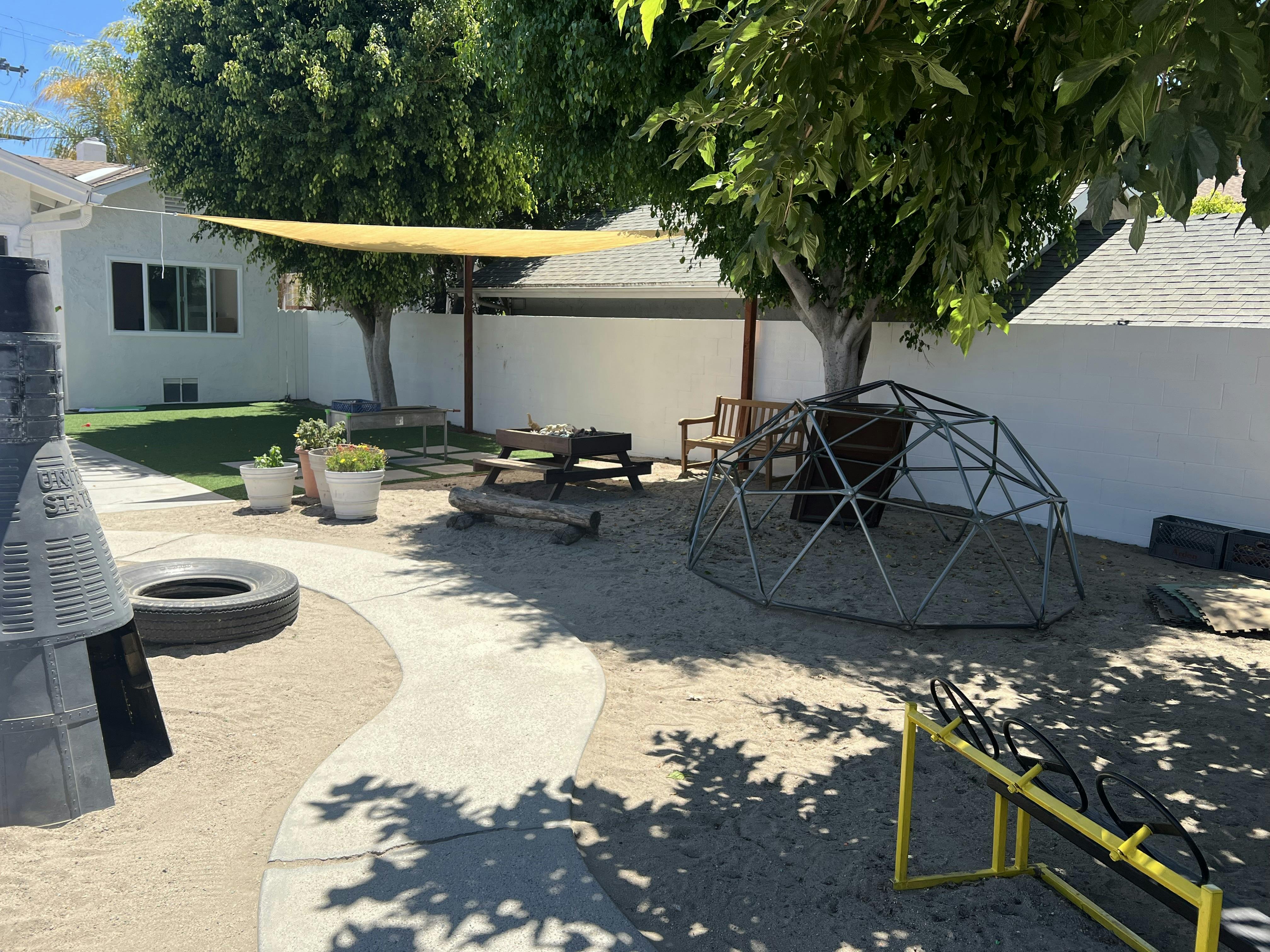 Outdoor play area with a geodesic dome, picnic table, and shade sail