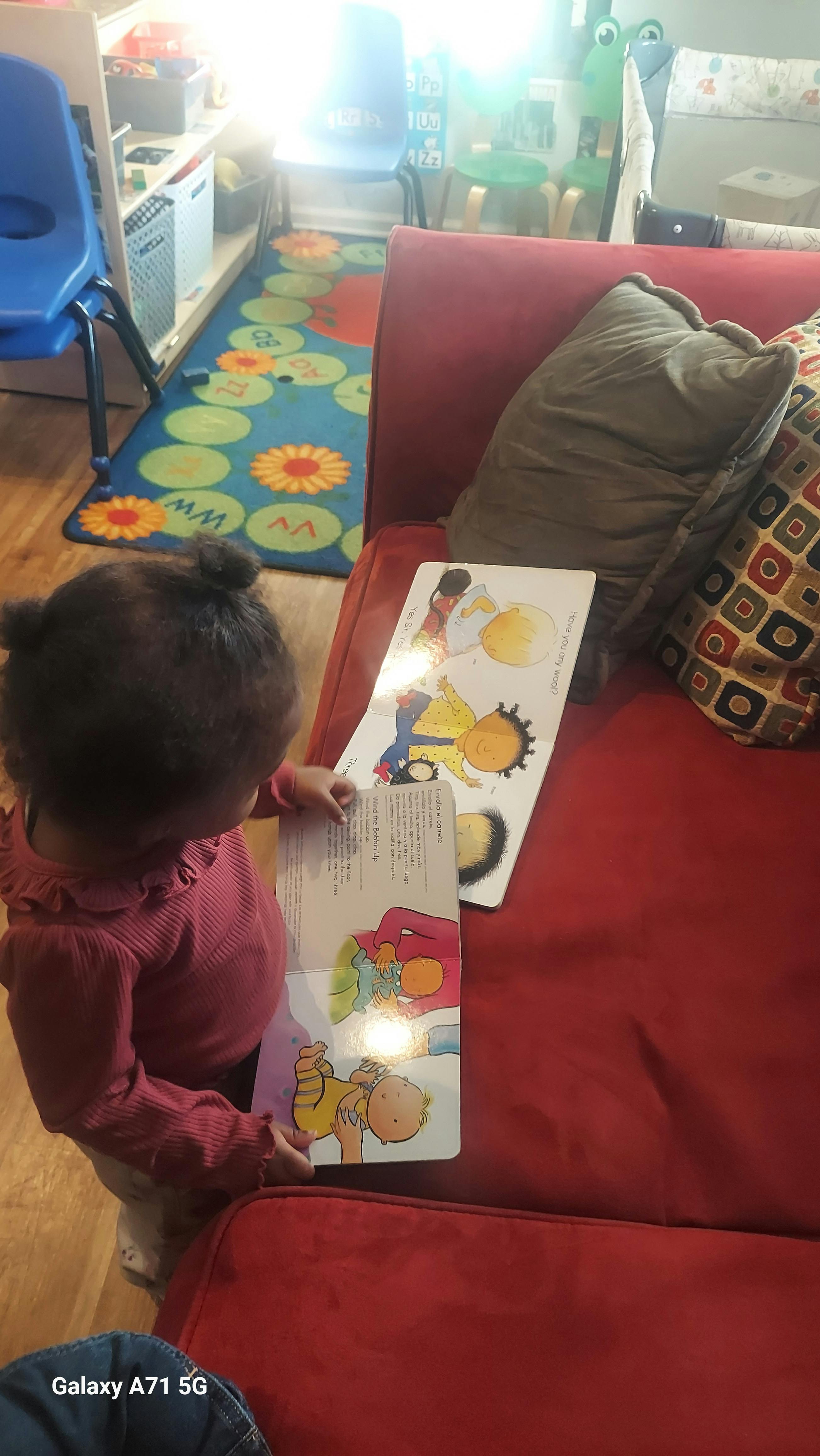 Child standing and looking at an open book on a red couch