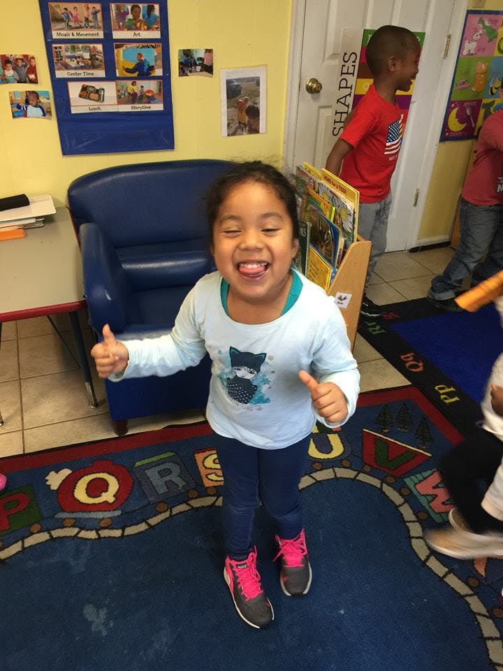 Child sticking out tongue and giving two thumbs up in a classroom