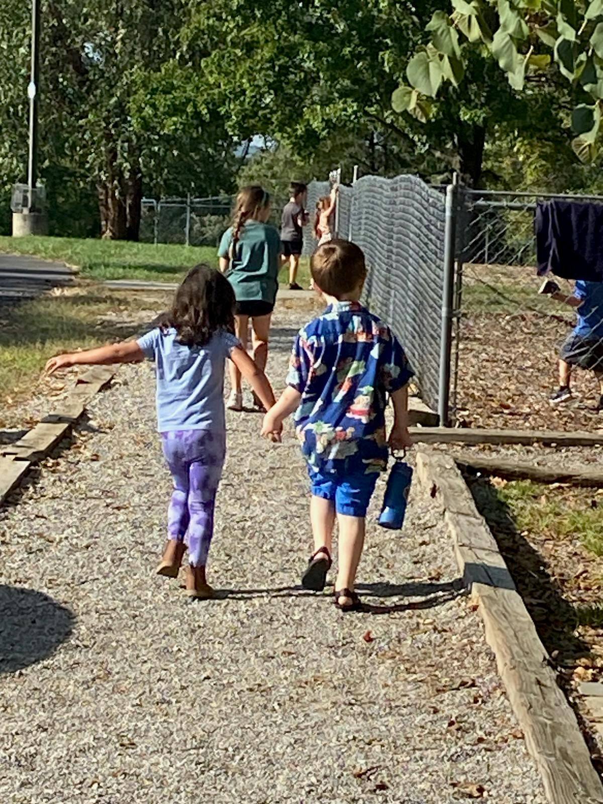 A child in purple leggings and a child in blue shorts holding hands on a gravel path