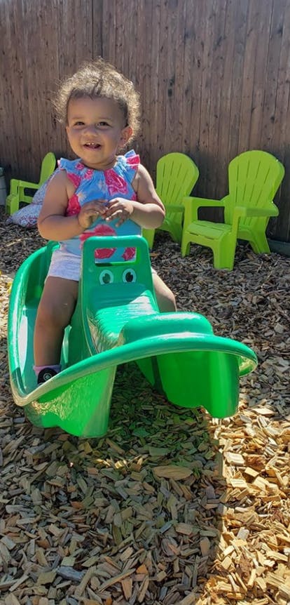 Child sitting on a green plastic seesaw on wood chips
