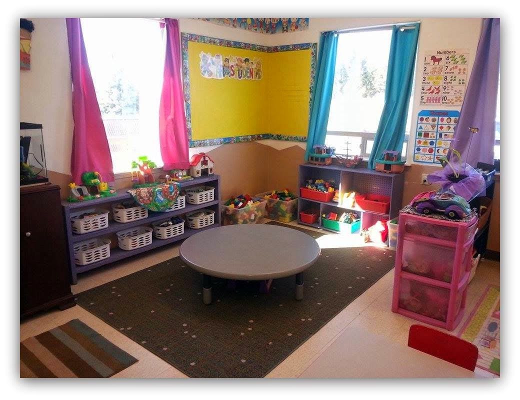 Classroom with a round table, shelves of toys, and colorful curtains