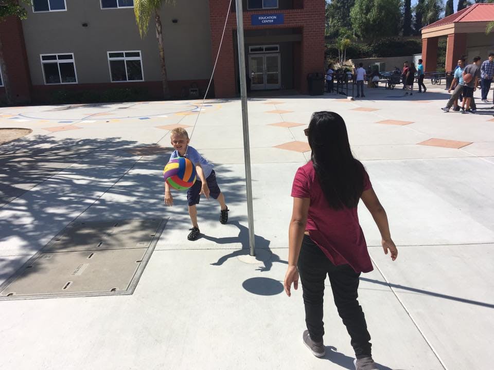 Child playing with a ball near a person in an outdoor area