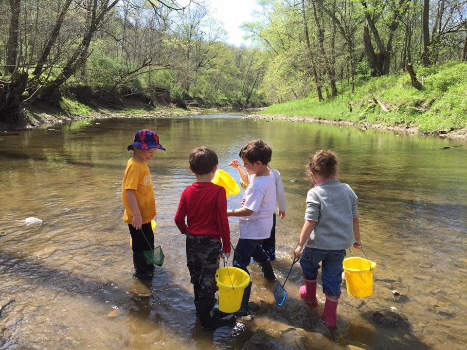 Four children standing in a shallow stream with buckets