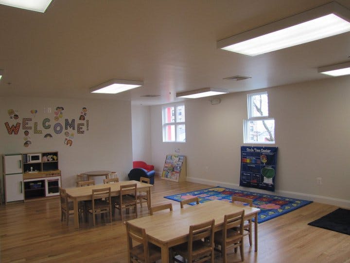 Empty classroom with small tables and chairs, play kitchen, and colorful rug