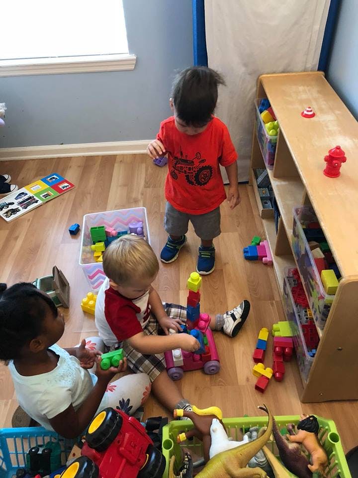 Three children playing with toys on a wooden floor