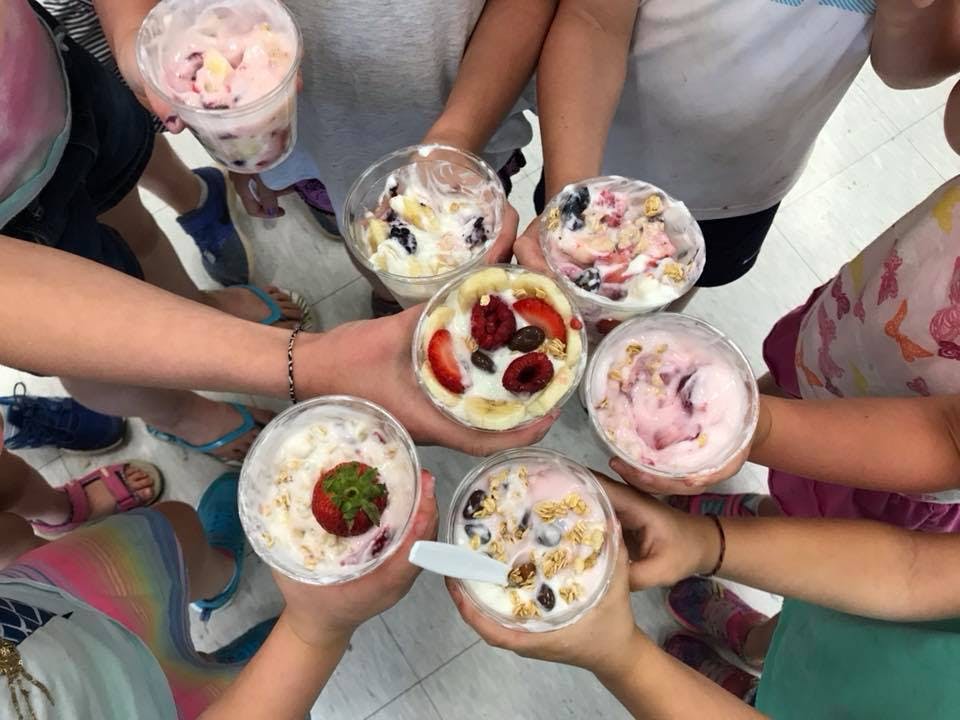 People holding cups of yogurt parfaits with fruit and granola