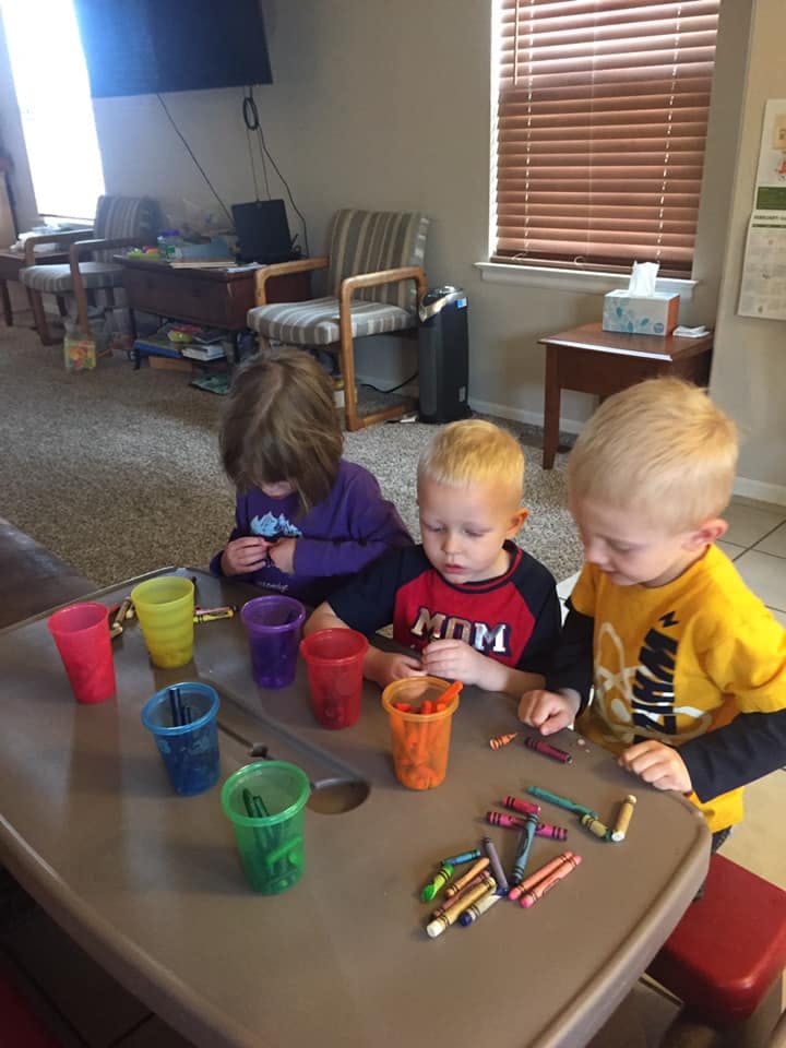 Three children playing with crayons and colorful cups at a table