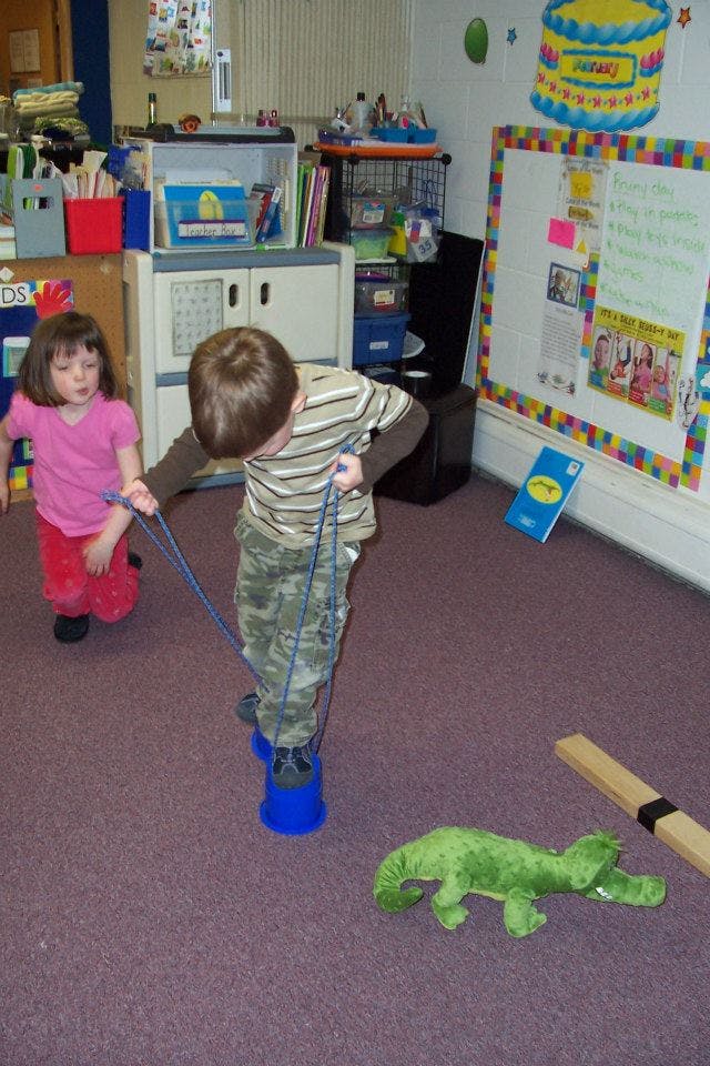 Child on stilts with another child nearby in a classroom